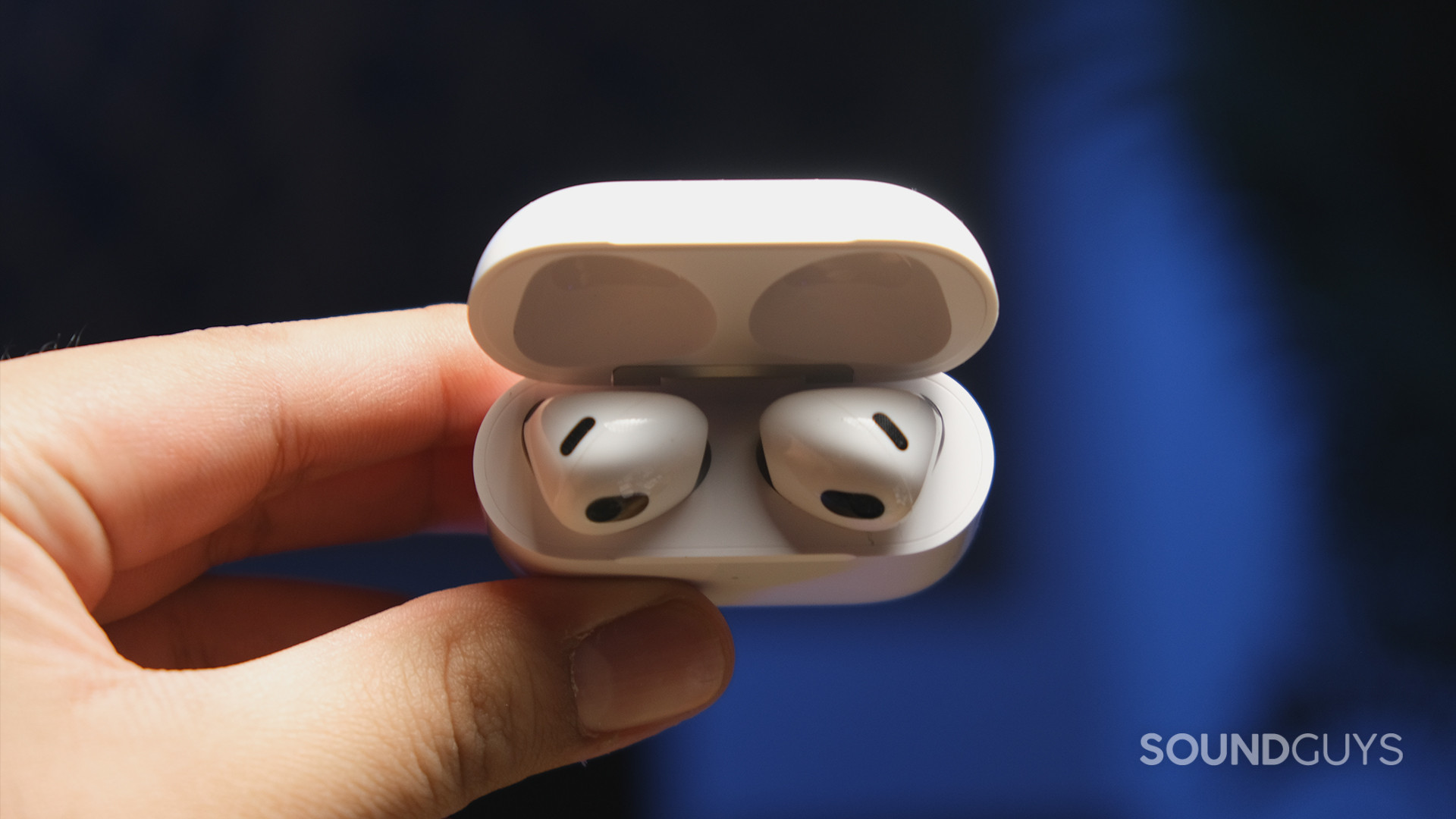 A hand holds the Apple AirPods (3rd generation) case at an angle to display shape of the earbuds.