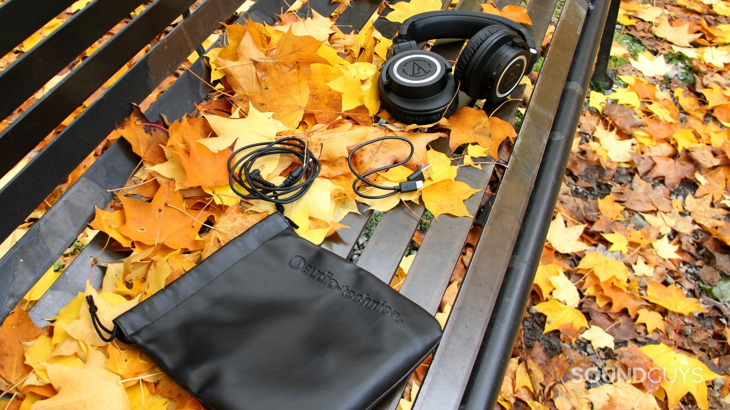 Audio-Technica ATH-M50xBT2 with pouch, USB cable, and headphone jack cable on a bench.