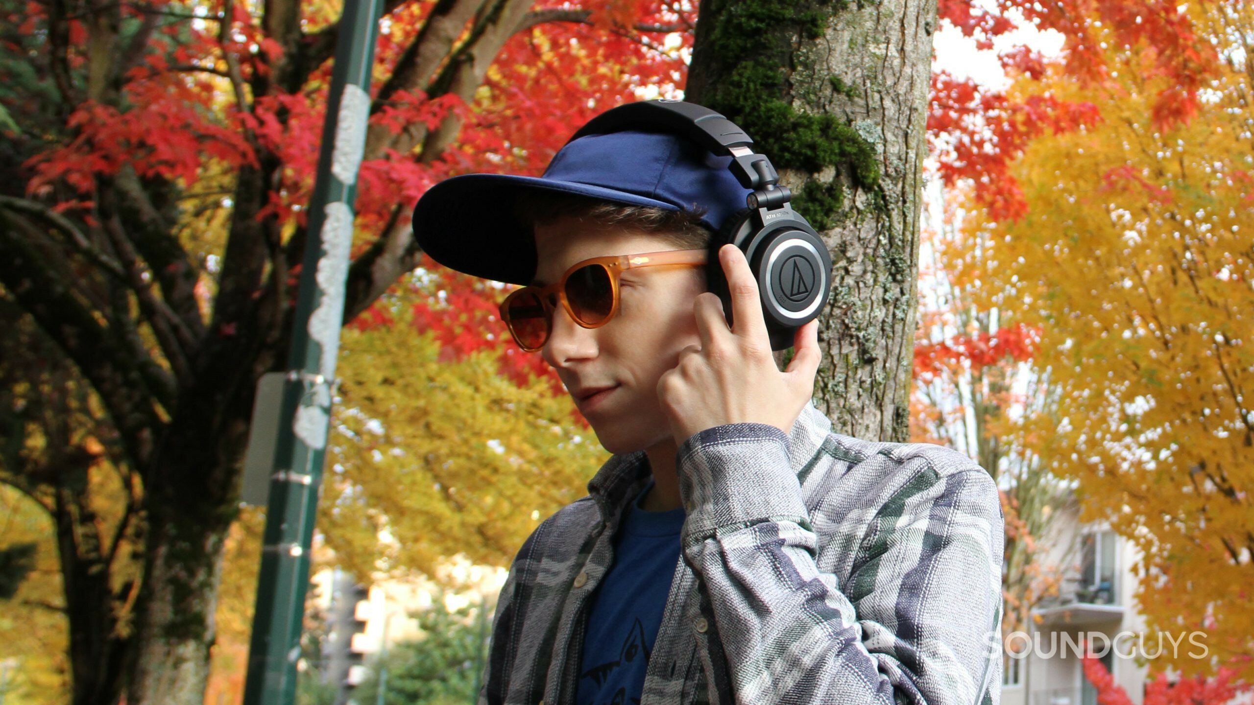 A man wears the Audio-Technica ATH-M50xBT2 pressing the buttons on the left ear cup.