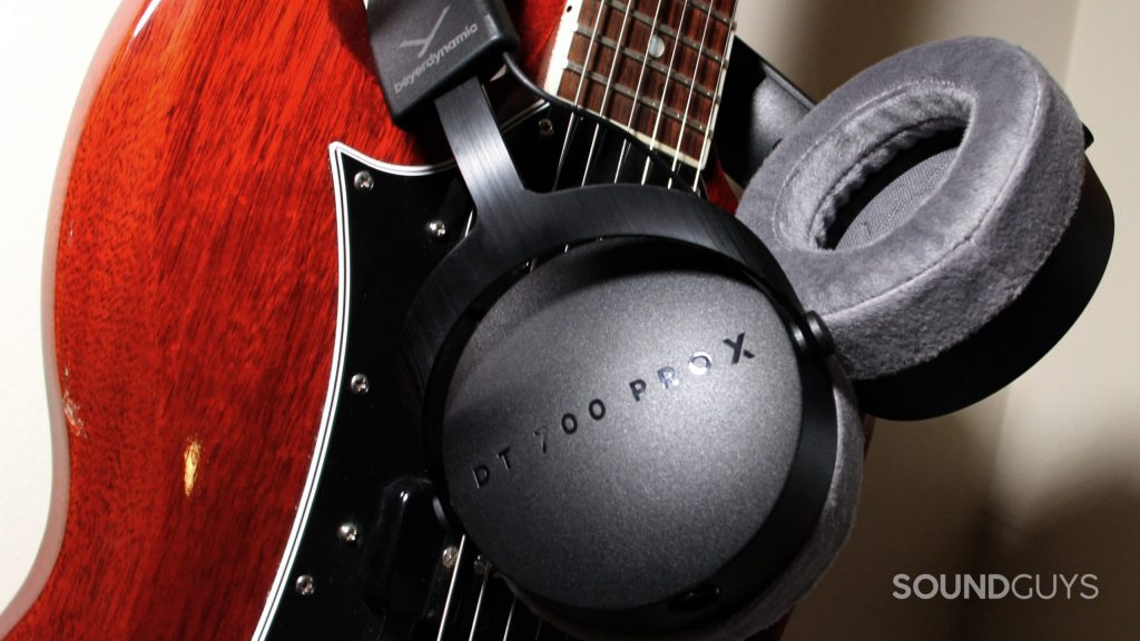 Around the neck of a red guitar the Beyerdynamic DT 700 Pro X is slung over, showing the ear cups.