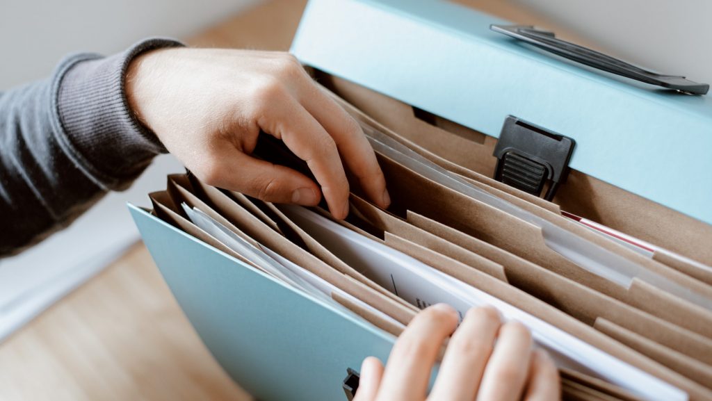 A pair of hands opens a collection of folders with documents.