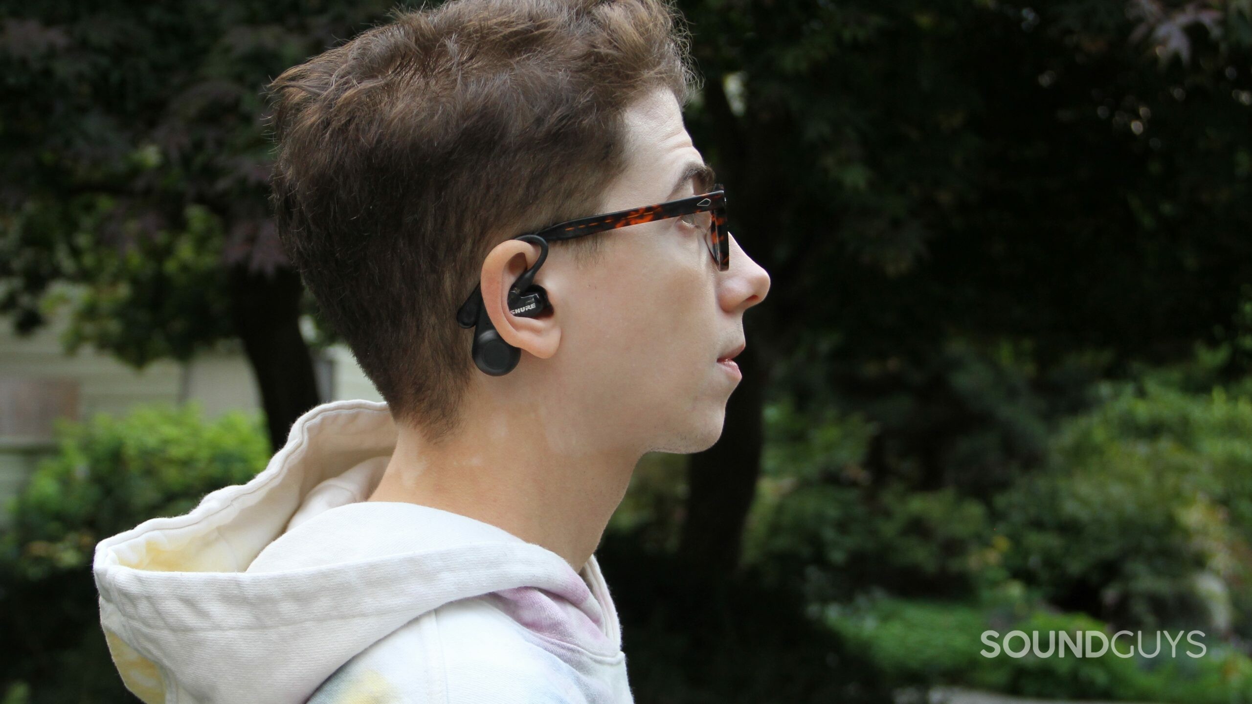 The profile of a man facing right wearing the Shure AONIC 215 Gen 2 with trees and bushes in the background.