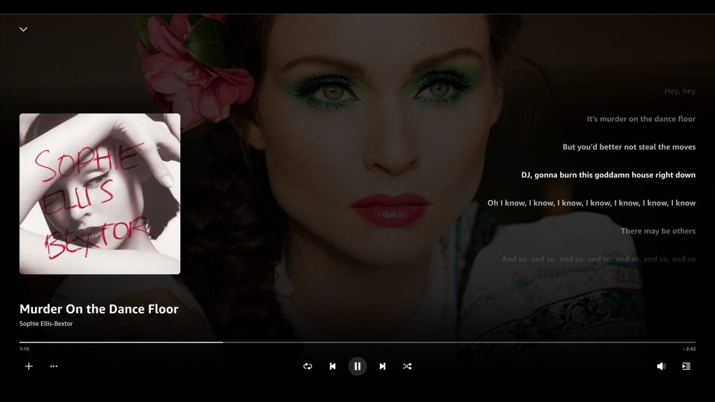 A screenshot of the Amazon Music web player showing the album art of Sophie Ellis-Bextor's "Murder on the Dance Floor" and the current lyrics from 1:10 in the song which read: "Hey, hey It's murder on the dancefloor / But you better not steal the moves / DJ, gonna burn this goddamn house right down / Oh I know, I know, I know, I know, I know, I know / There may be others / And so, and so, and so, and so, and so, and so..." In the background is the artist's face with colorful makeup on and a flower in her hair.