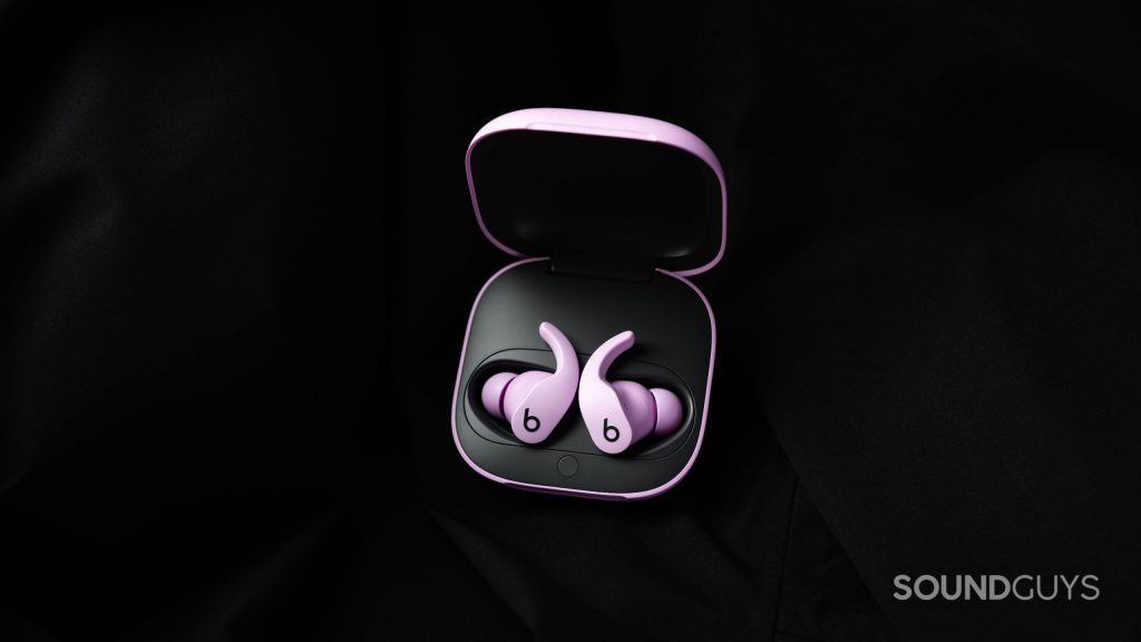 The Beats Fit Pro noise cancelling true wireless earbuds in purple lay in the open charging case against a black fabric background.