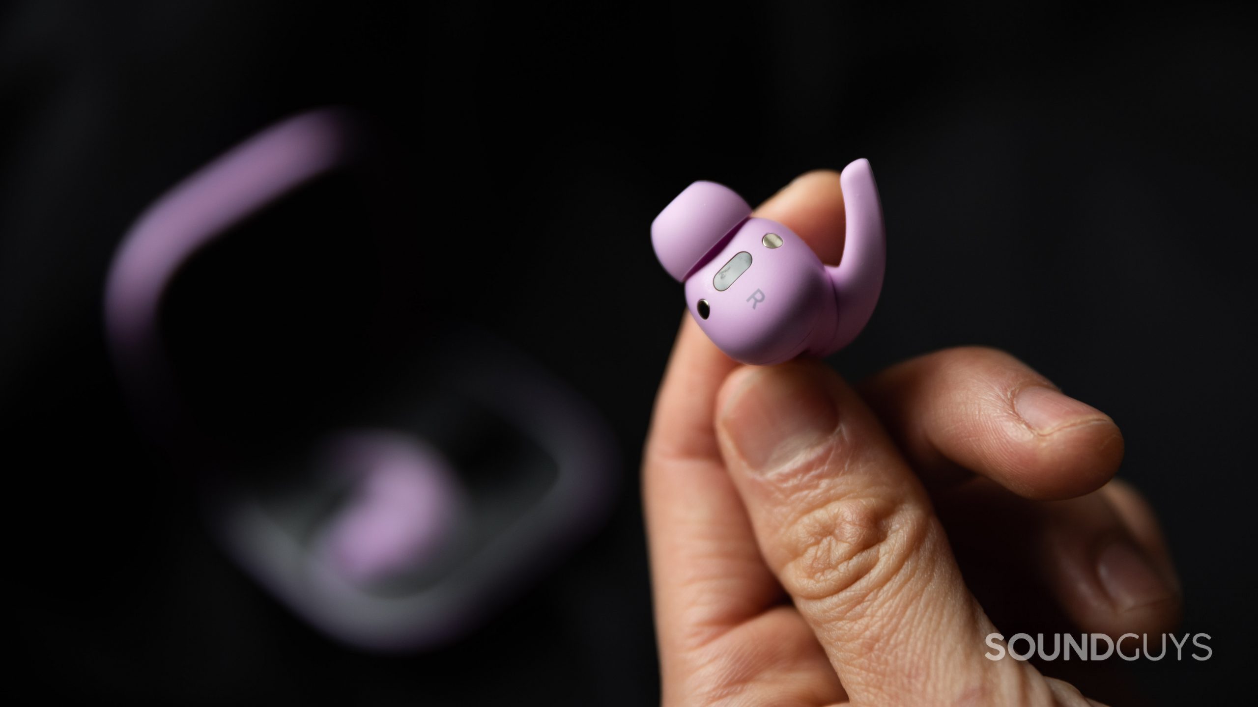 A hand holds the Beats Fit Pro noise canceling true wireless earbud in purple to display its sensors, magnets, and wing tip extension.