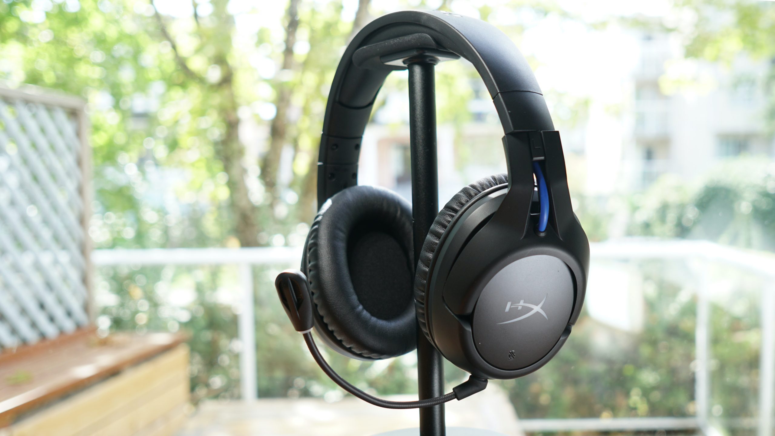 The HyperX Cloud Flight Wireless sits on a headphone stand in front of a window.