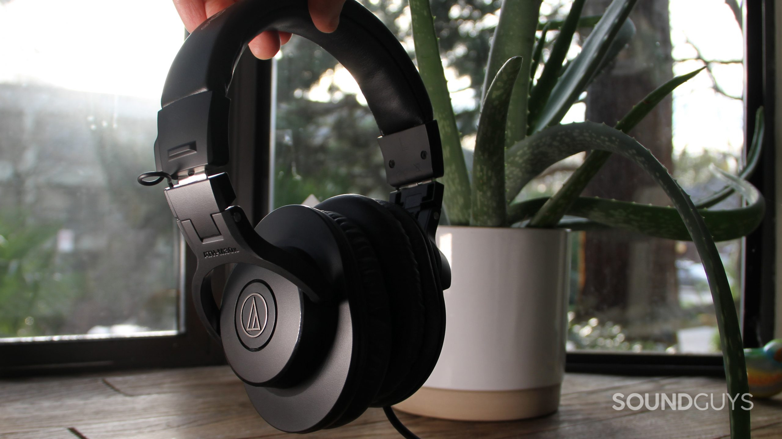 A hand holds the Audio-Technica ATH-M30x in front of a window and an aloe plant.