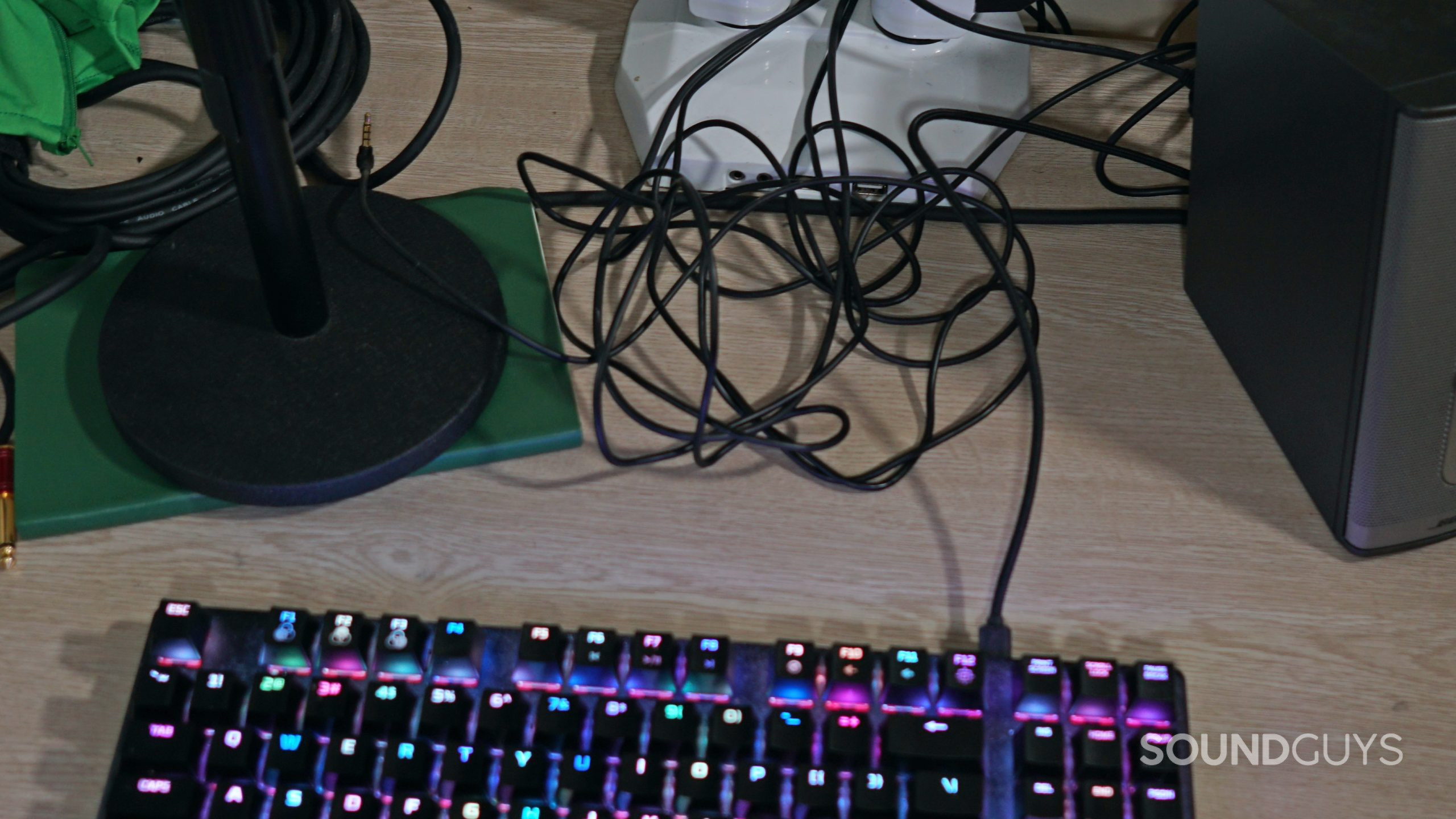A keyboard and wires tanged up on a wooden desk.