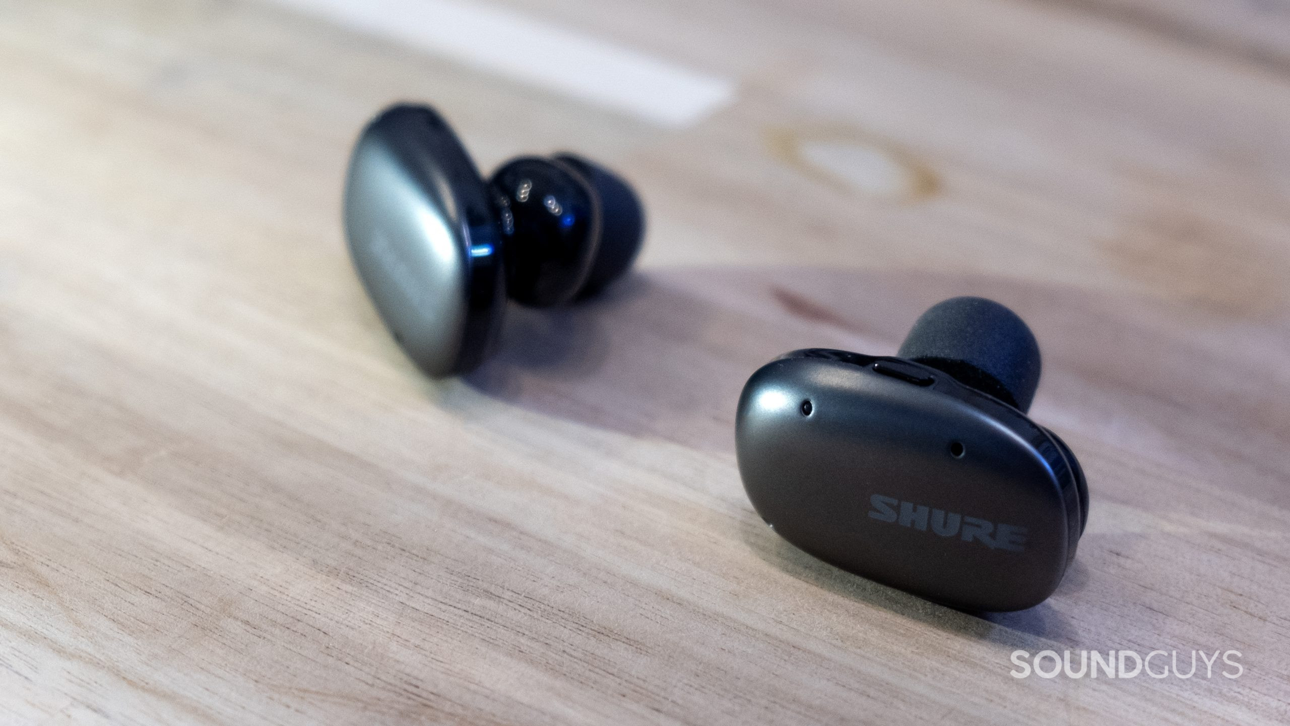 A close up of the Shure AONIC Free earbuds on a light wood surface.