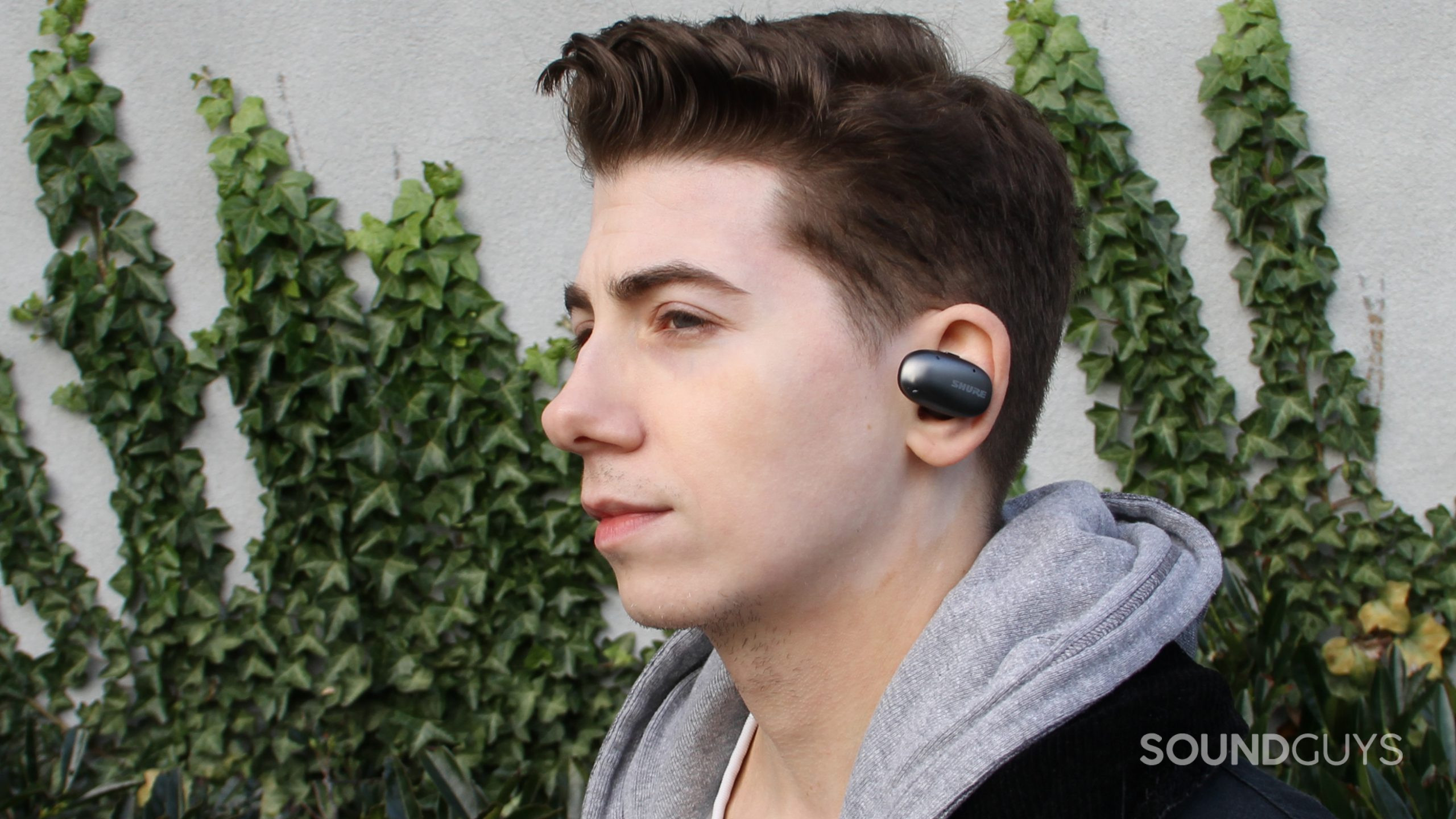 A man wears the Shure AONIC Free earbuds looking left with ivy in the background.