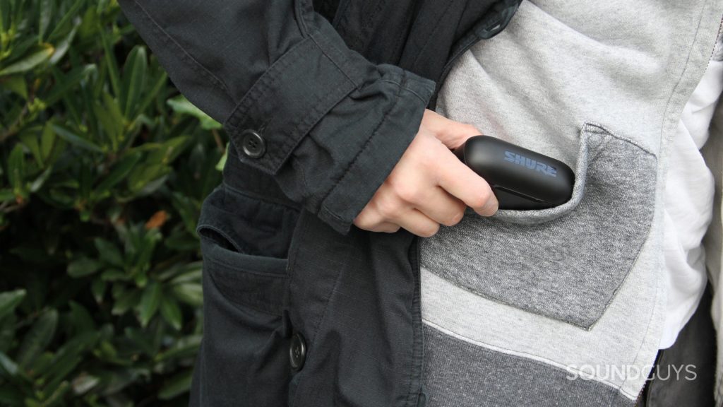 A hand holds the case of the Shure AONIC Free and places it into a pocket of a hooded sweatshirt.