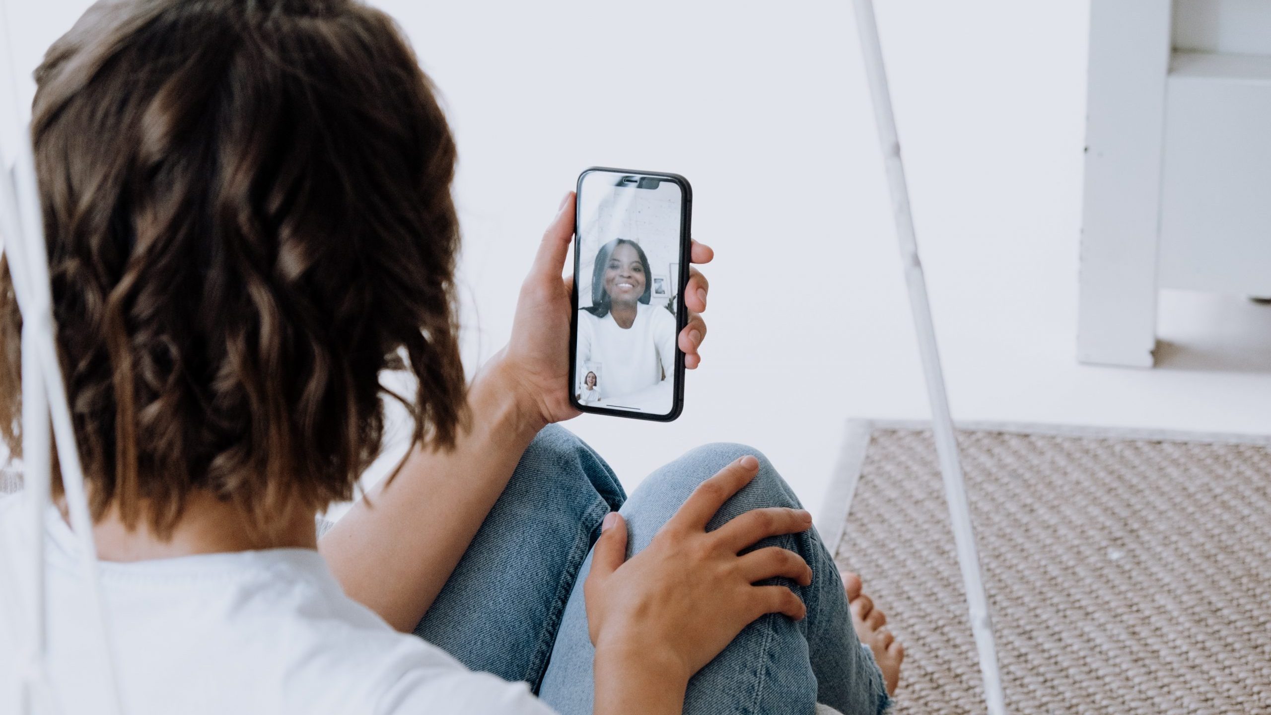 A woman sits on steps as she uses an iPhone to FaceTime a friend.