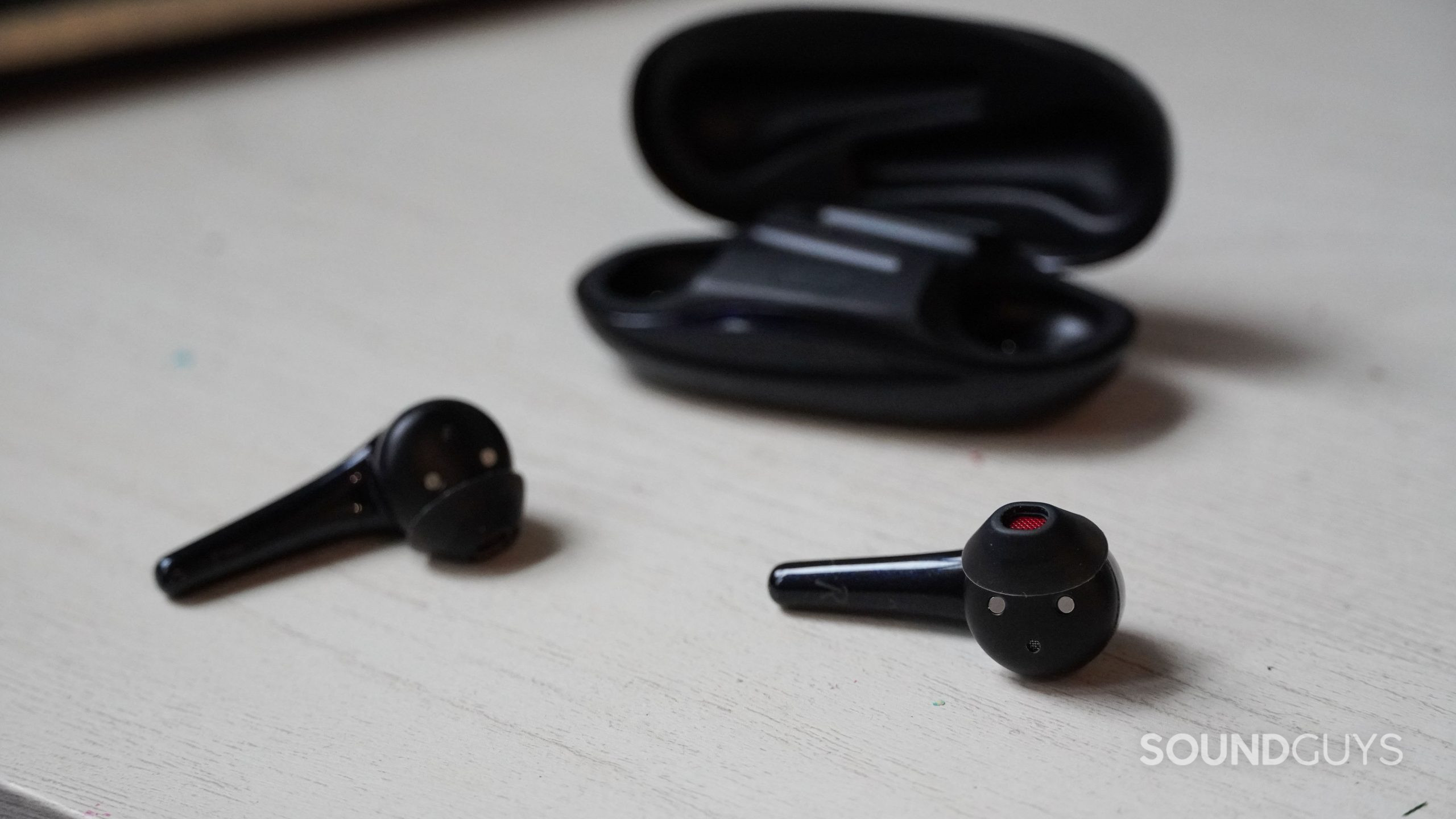 The 1MORE Comfobuds 2 earbuds and case on an off-white table.