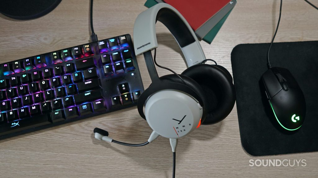 The Beyerdynamic MMX 150 gaming headset lays on a desk between a Logitech gaming mouse and a HyperX mechanical gaming keyboard.