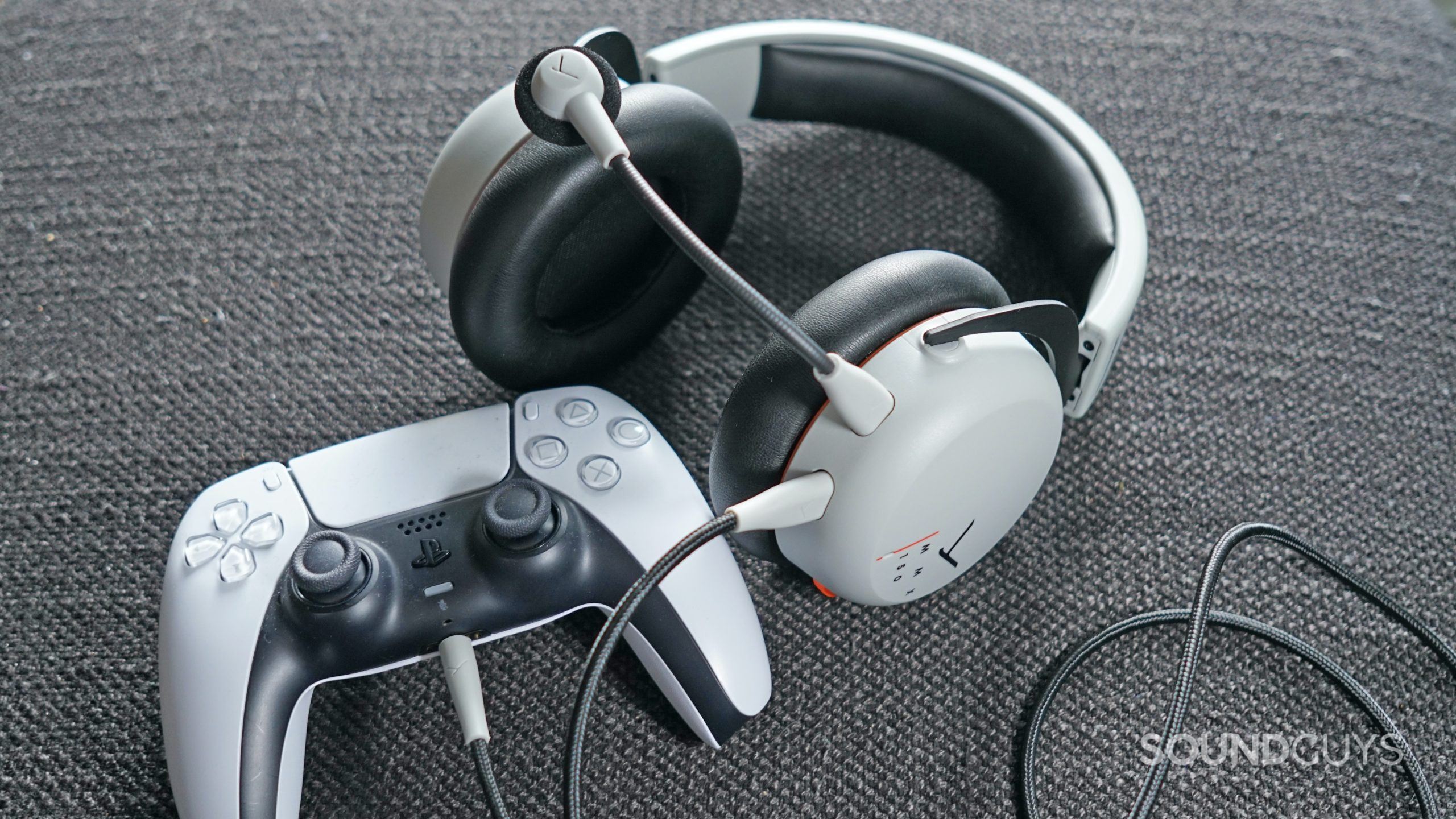 The Beyerdynamic MMX 150 lays on a fabric surface plugged into a PlayStation DualShock 5 controller.