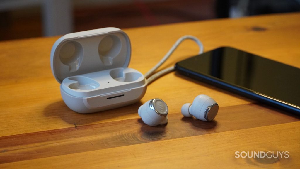 The JBL Reflect Flow Pro earbuds and case on a wooden table next to an iPhone 7 Plus.