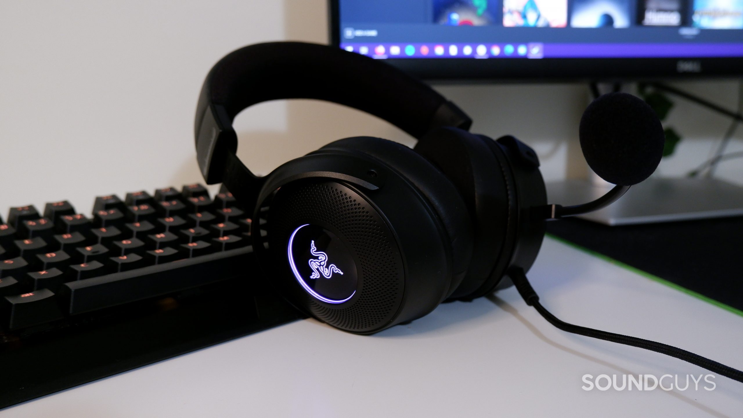 Razer Kraken V3 headset resting against a keyboard, with a computer screen in the background.