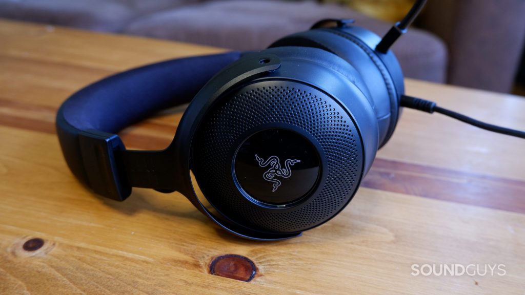 A Razer Kraken V3 headset resting on a wooden table, showing its logo on the ear cup.