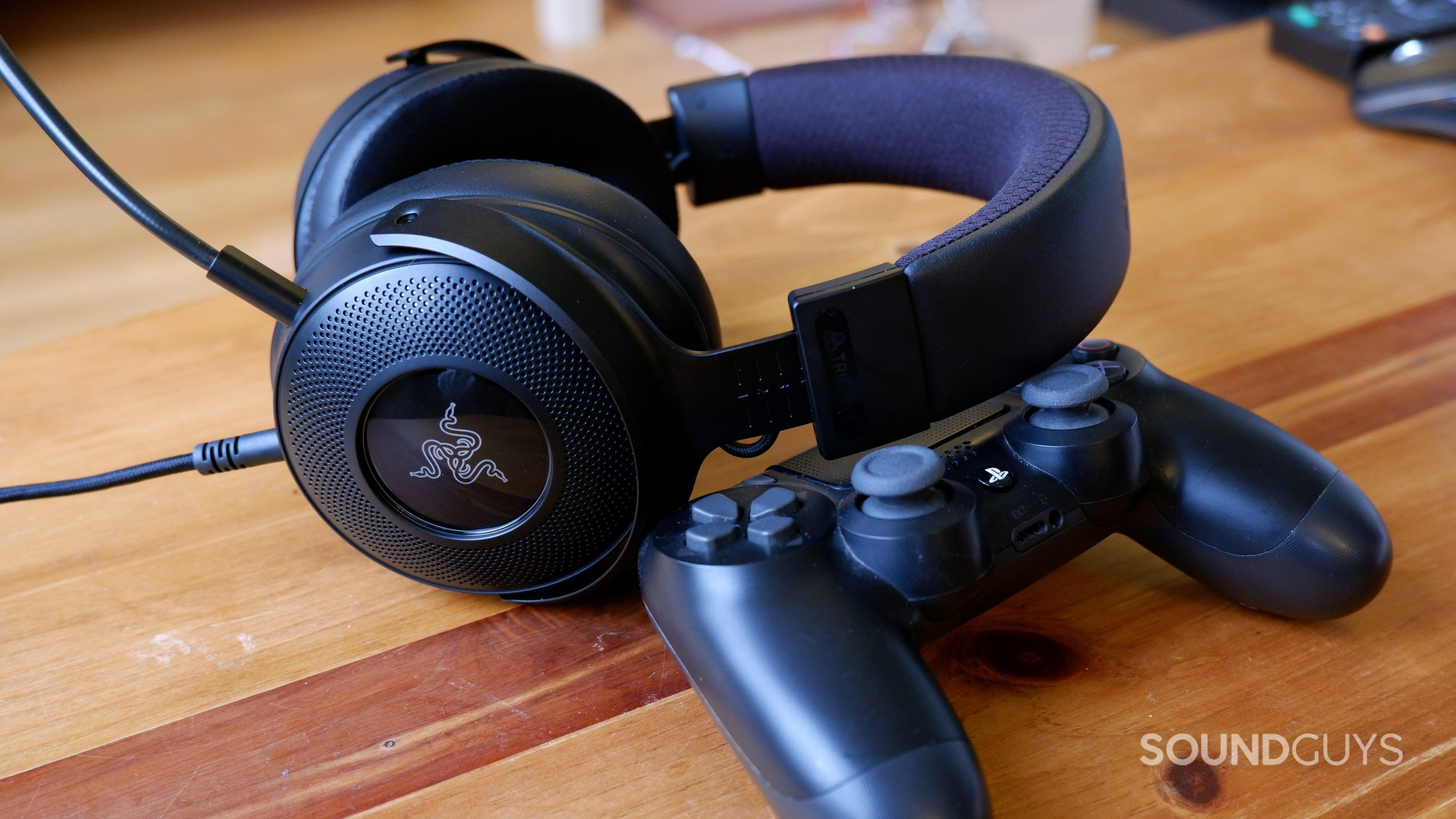 The Razer Kraken V3 headset resting against a PlayStation 4 controller on a wooden table.