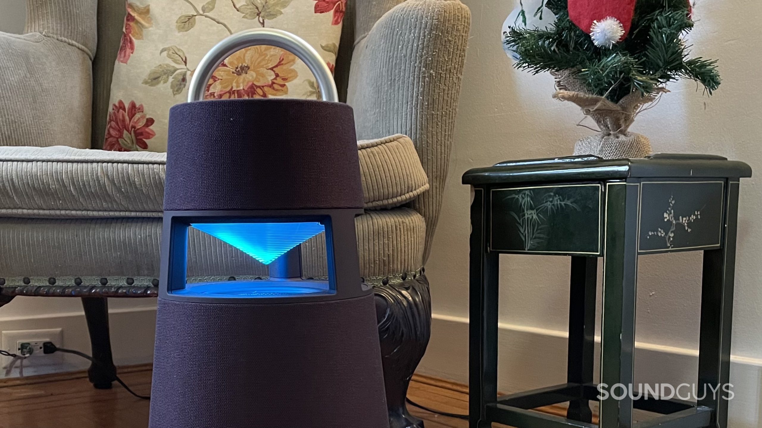 LG XBOOM 360 with an armchair, side table, and small Christmas tree in the background.
