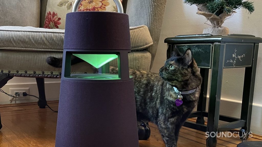 The LG XBOOM 360 resting on the floor with a cat gazing at its glowing lantern.