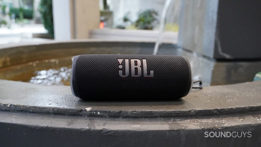 A JBL Flip 6 Bluetooth speaker sitting next to a small fountain.