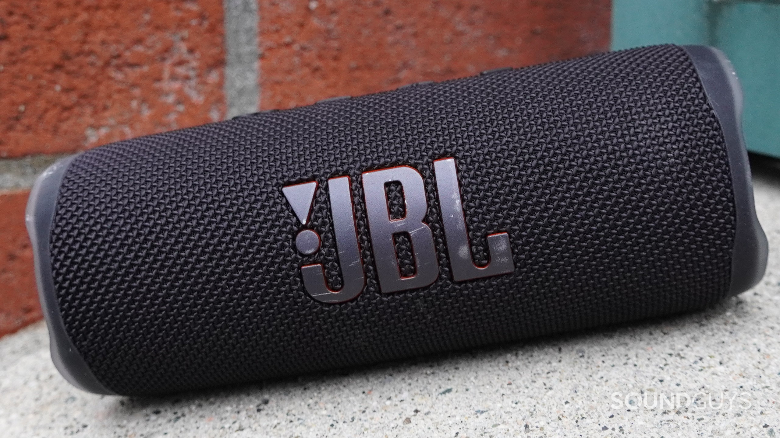 A JBL Flip 6 sittin on an inclied surface next to a brick wall.