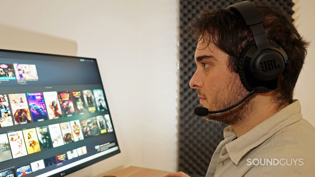 JBL Quantum 350 Wireless on a man's head while he is looking at a desktop monitor running Steam with games like Resident Evil 7 and Battlefield 1 on it.