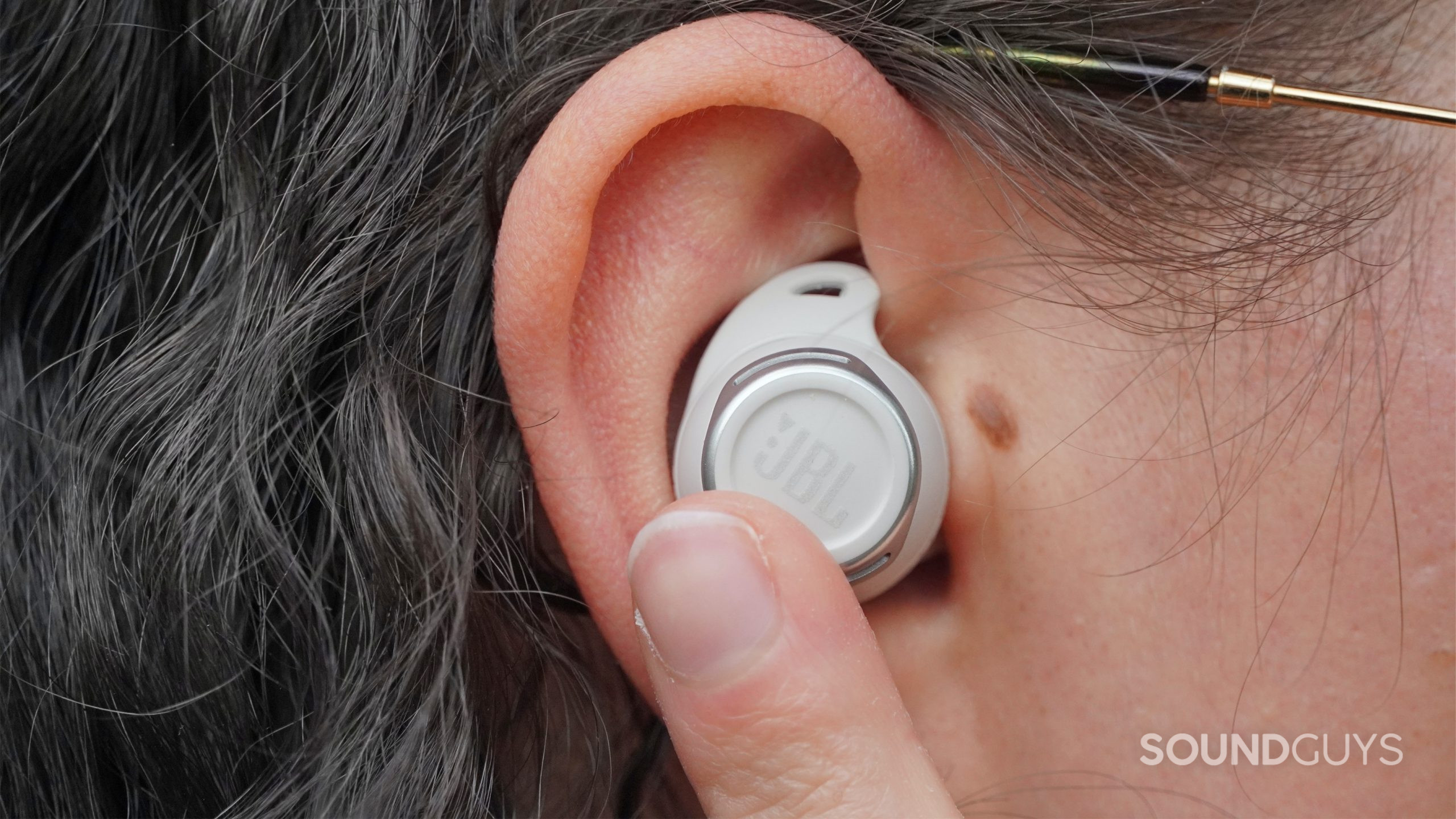 A JBL Reflect Flow Pro earbud in a person's ear, with their finger gesturing towards it.