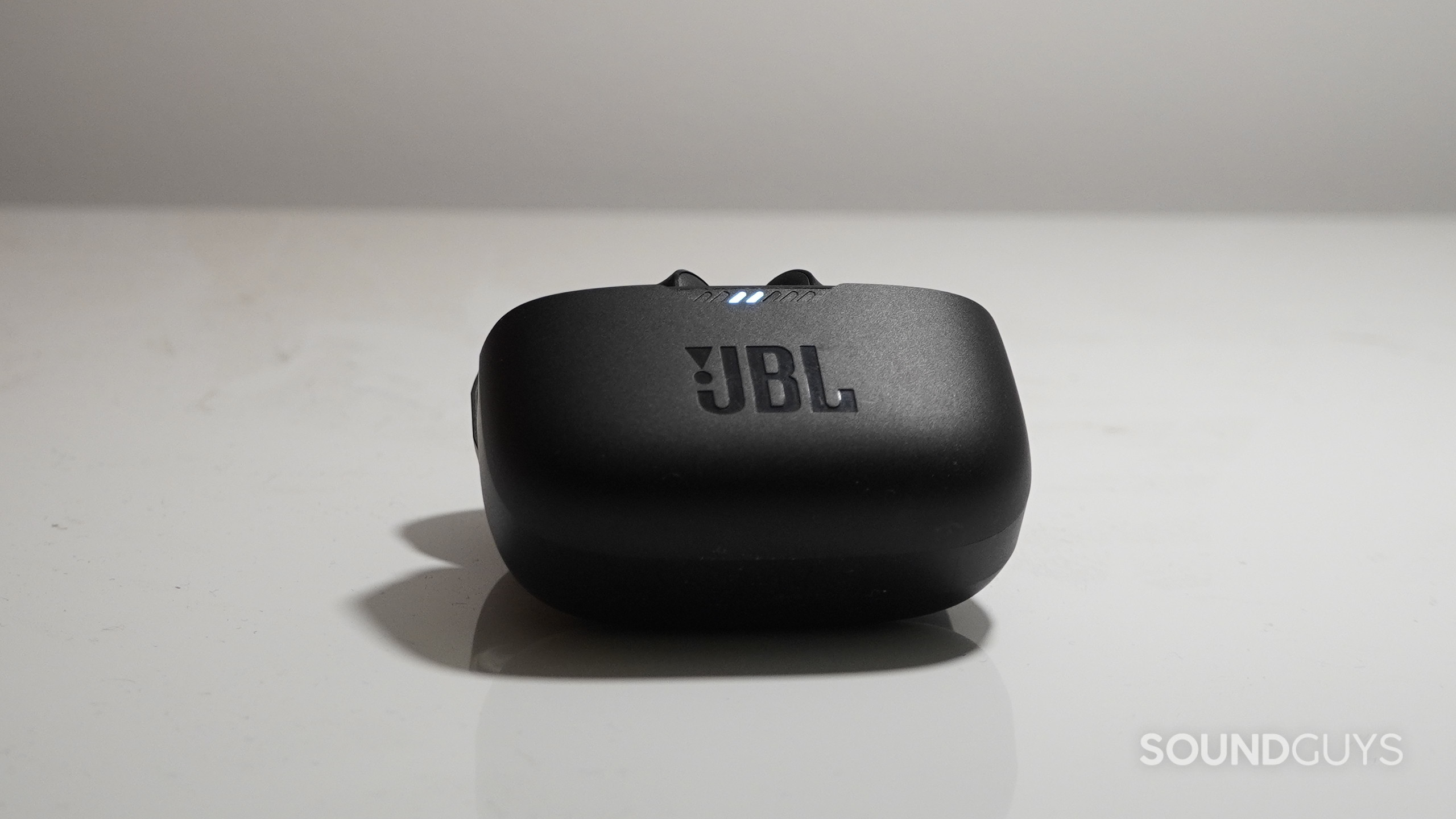 The The JBL Tunes 230NC TWS charging case open and tipped backward lying on a white surface.