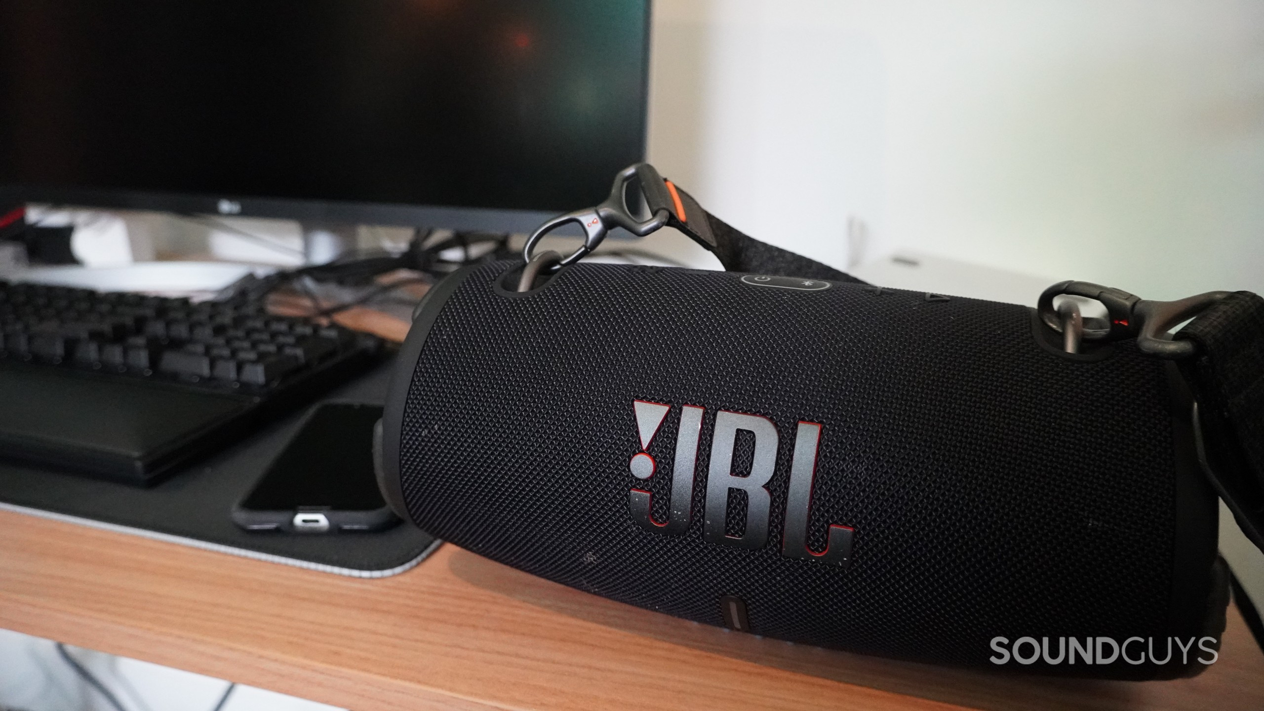 JBL-xtreme-3-bluetooth-multipoint The JBL Xtreme 3 Bluetooth speaker sitting on a desk next to a phone, keyboard, and computer monitor.