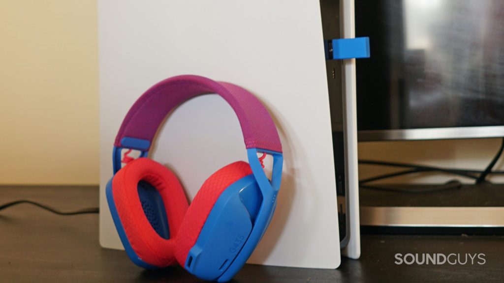 The Logitech G435 Lightspeed gaming headset leans up against a Sony PlayStation 5, with its USB dongle plugged in.