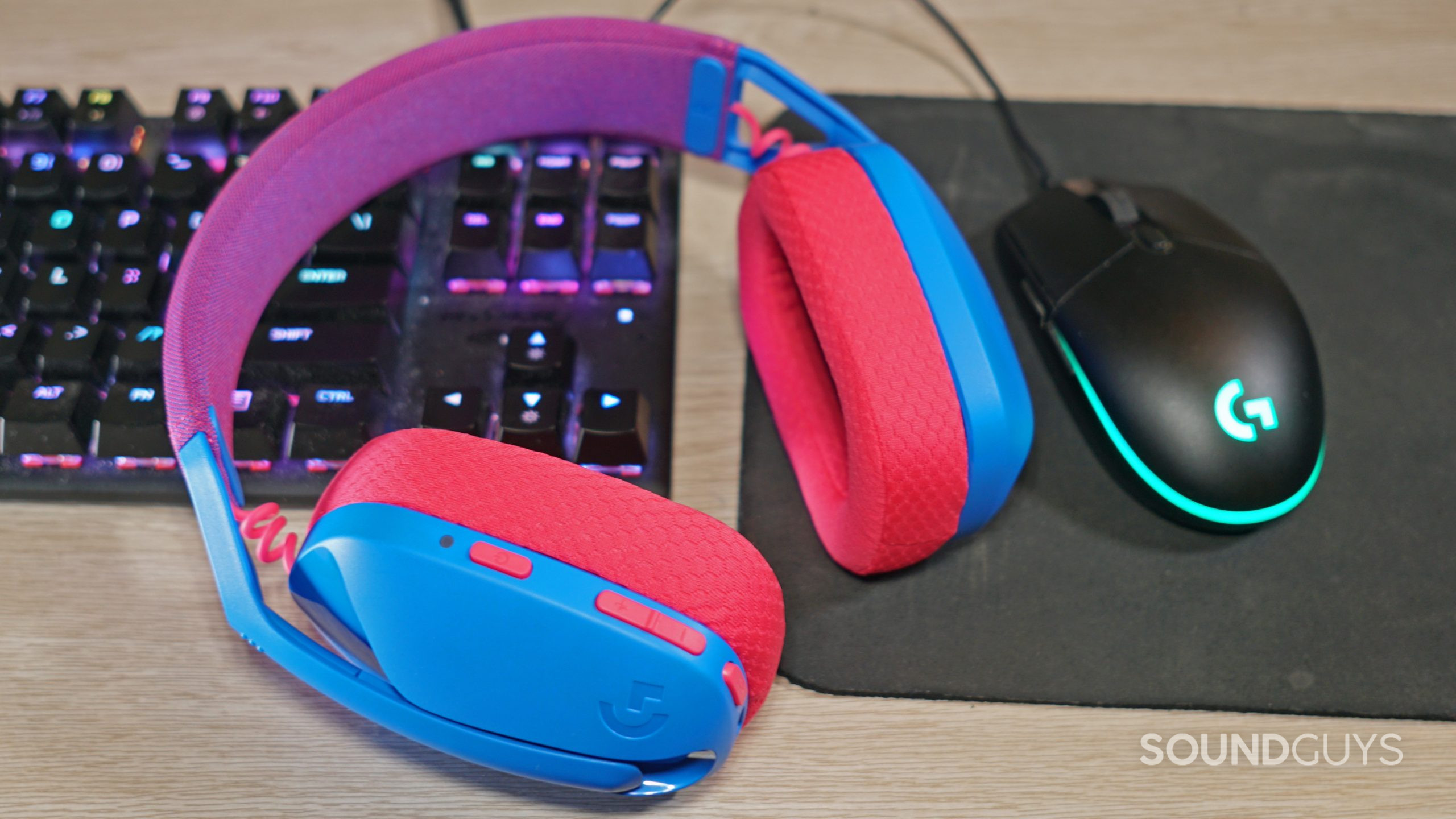 The Logitech G435 Lightspeed gaming headset lays on a desk next to a Logitech gaming mouse and a HyperX mechanical gaming keyboard.