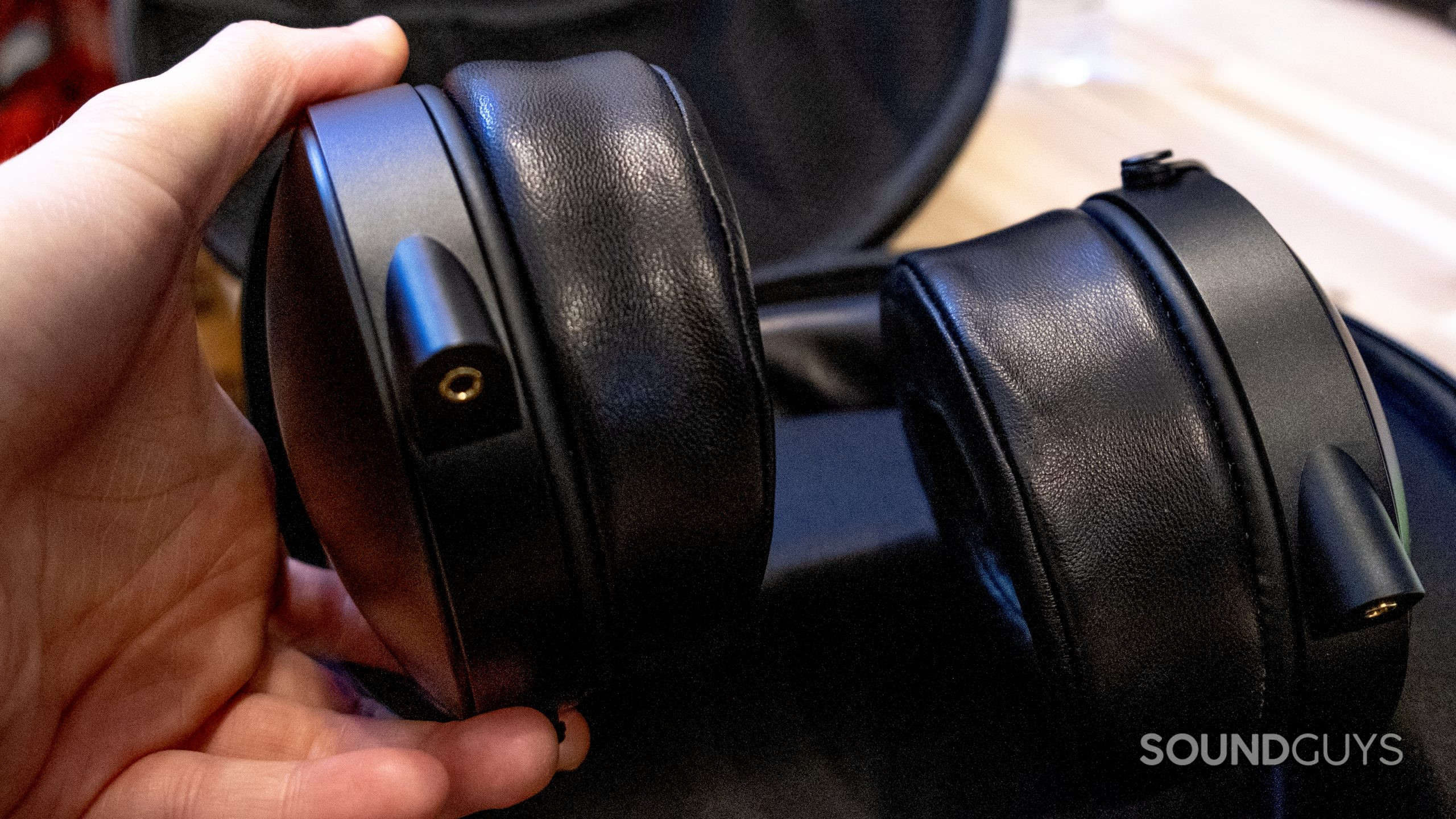 A hand holds up the bottom of the ear cup of the Monolith by Monoprice M1070C in its case.