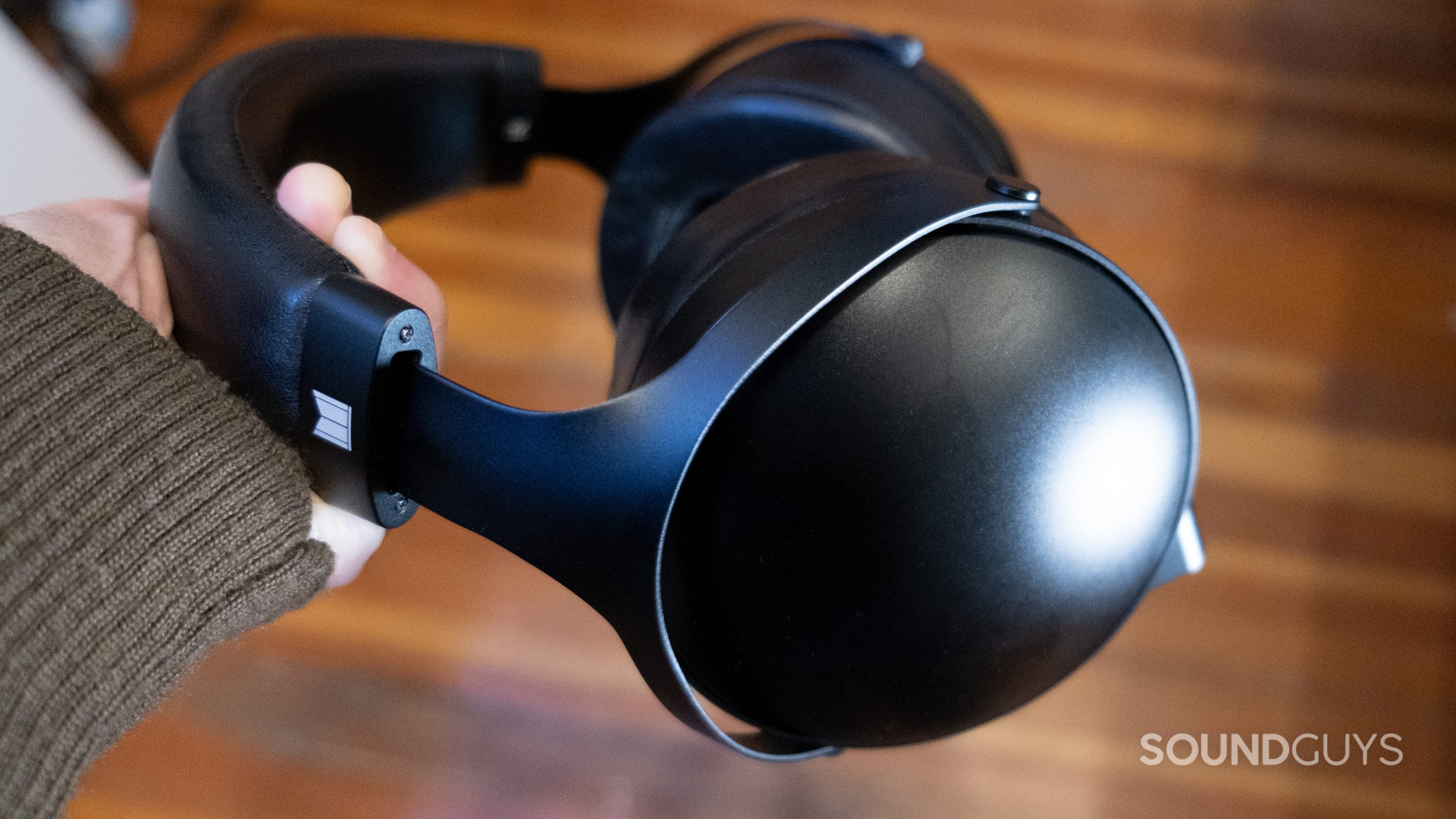 A hand holds the Monolith by Monoprice M1070C with a wooden floor in the background.