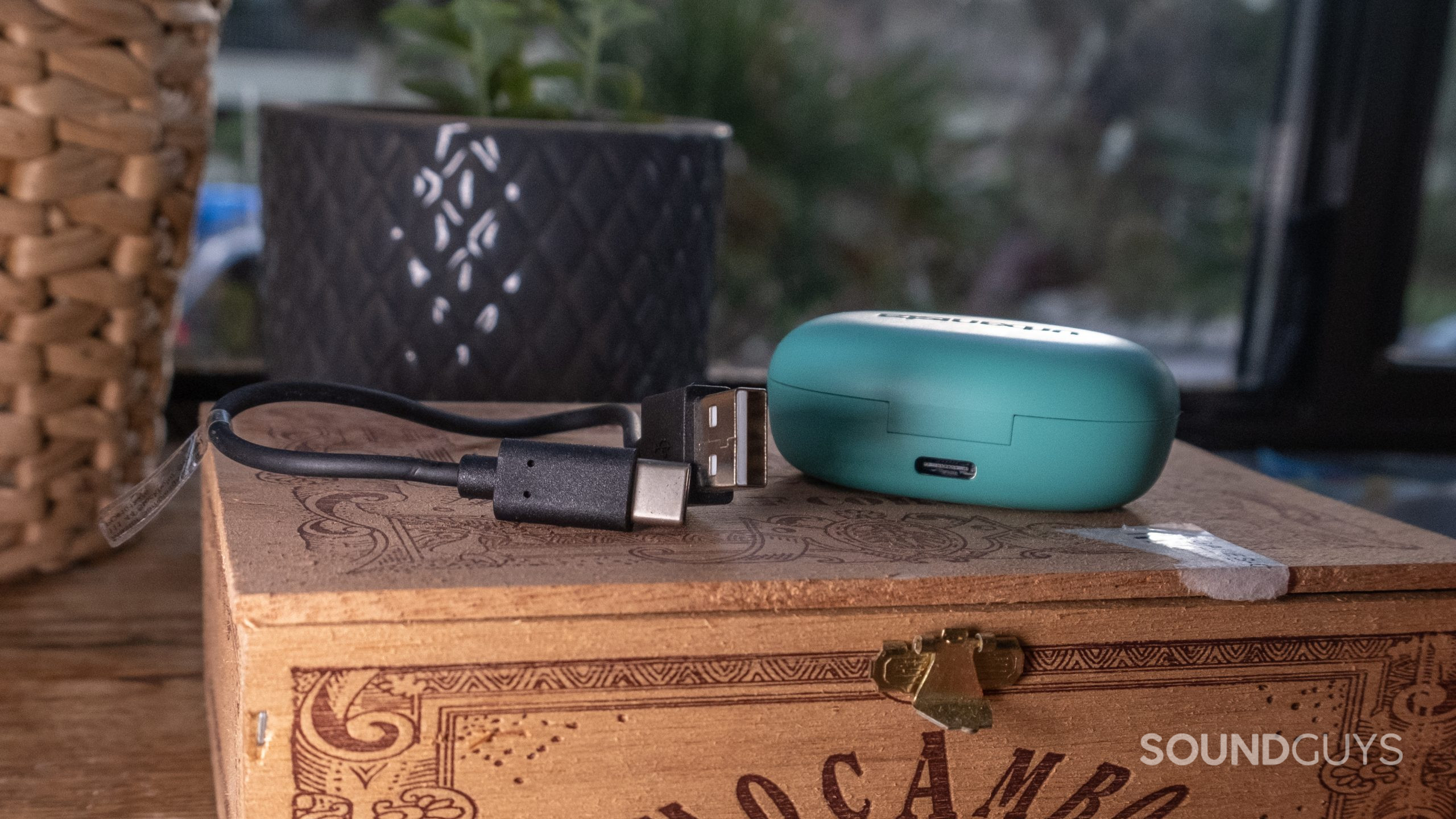 The included USB-C cable with the input on the case of the Urbanista Lisbon rest on a wood cigar box.