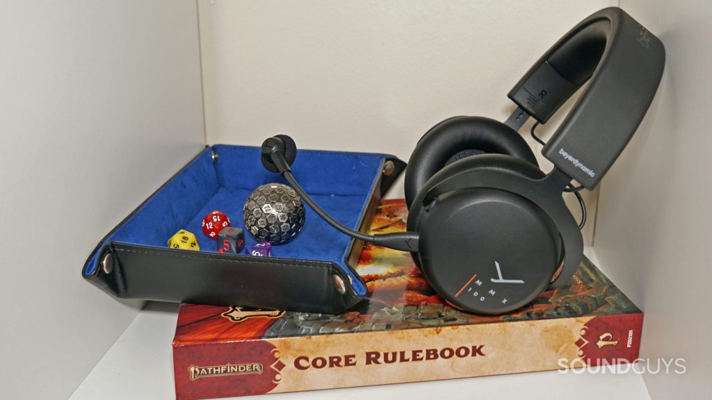 The Beyerdynamic MMX 100 sits on top of the Pathfinder Core Rulebook, next to a dice mat with different polyhedral dice on it.