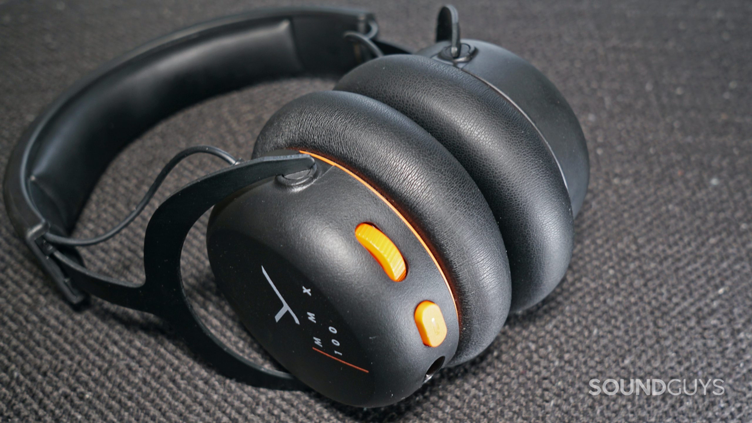 The Beyerdynamic MMX 100 gaming headset lays on a fabric surface with its volume dial and mute button in full view.