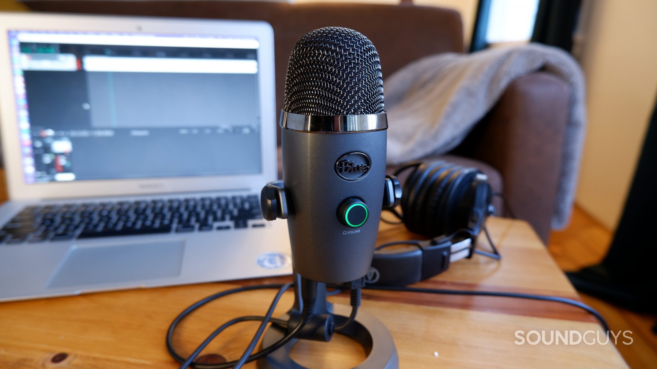 Blue Yeti Nano microphone sitting on a wooden table in front of a laptop and a pair of headphones.