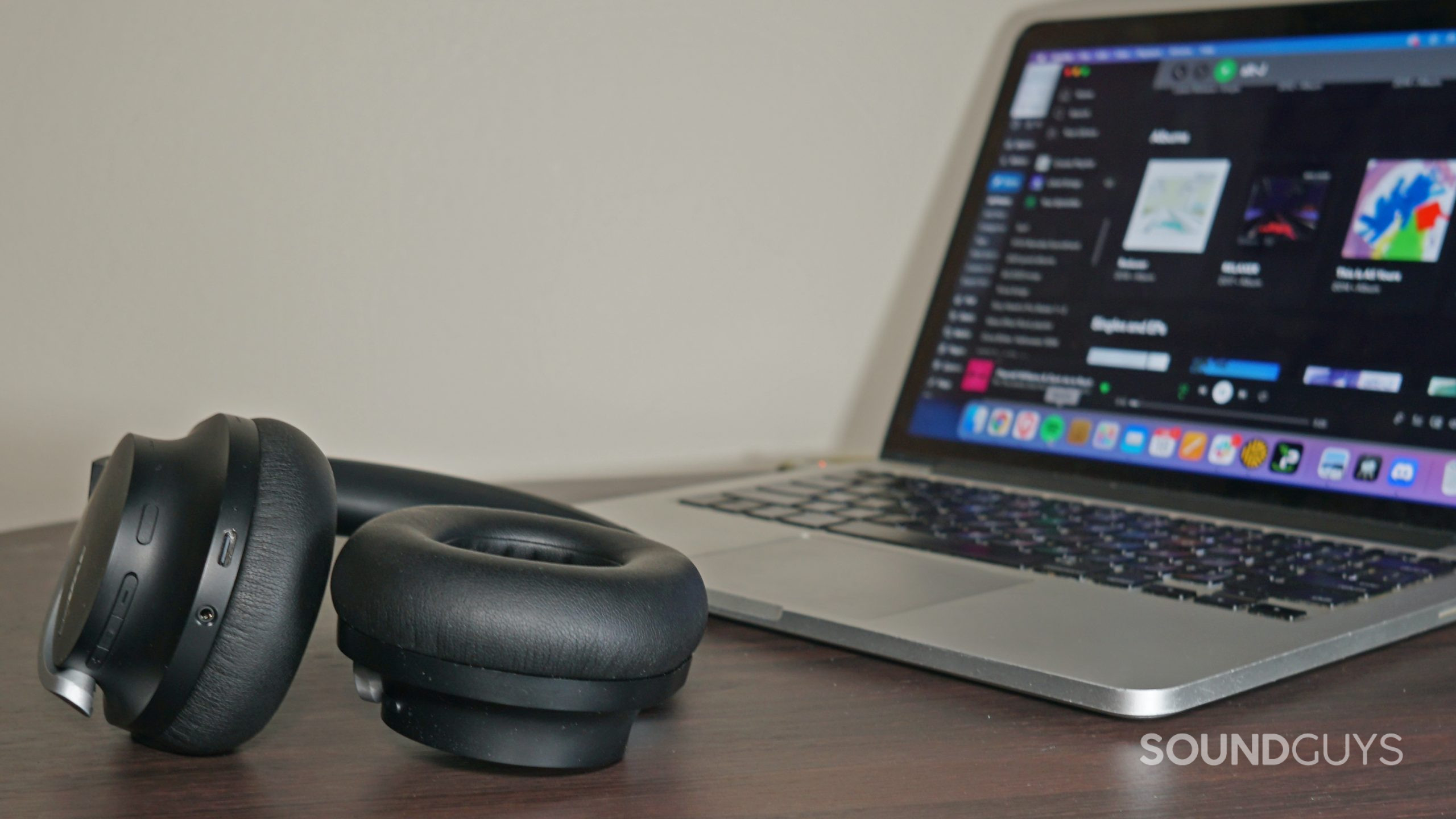 The Shure AONIC 40 bluetooth headphones lay on a wooden table next to an Apple MacBook Pro running Spotify.