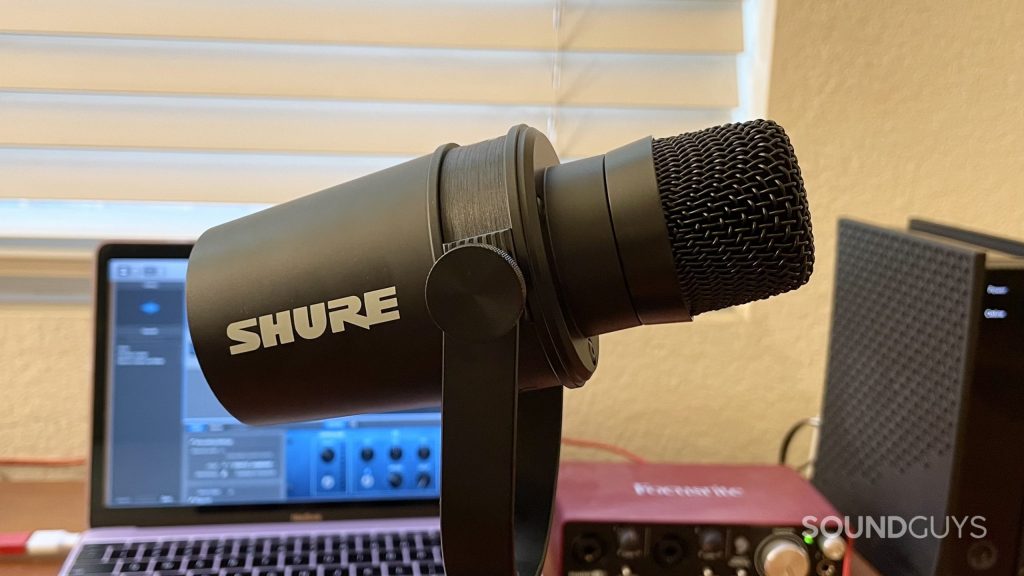Shure MV7X with the windscreen taken off. A laptop, audio interface, and WiFi modem are visible in the background.