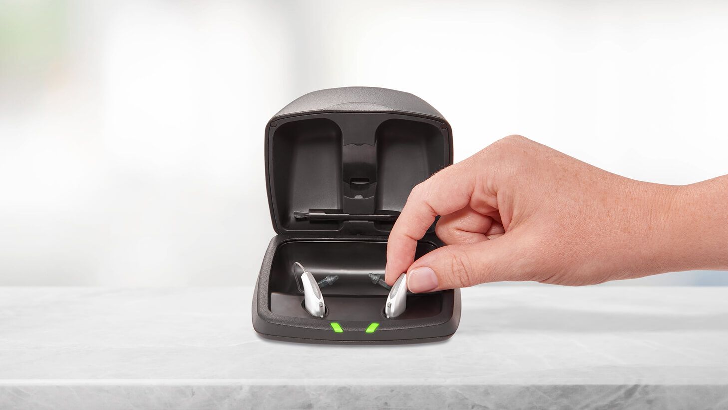 Hand putting a Starkey Livio Edge AI hearing aid into its charging case.