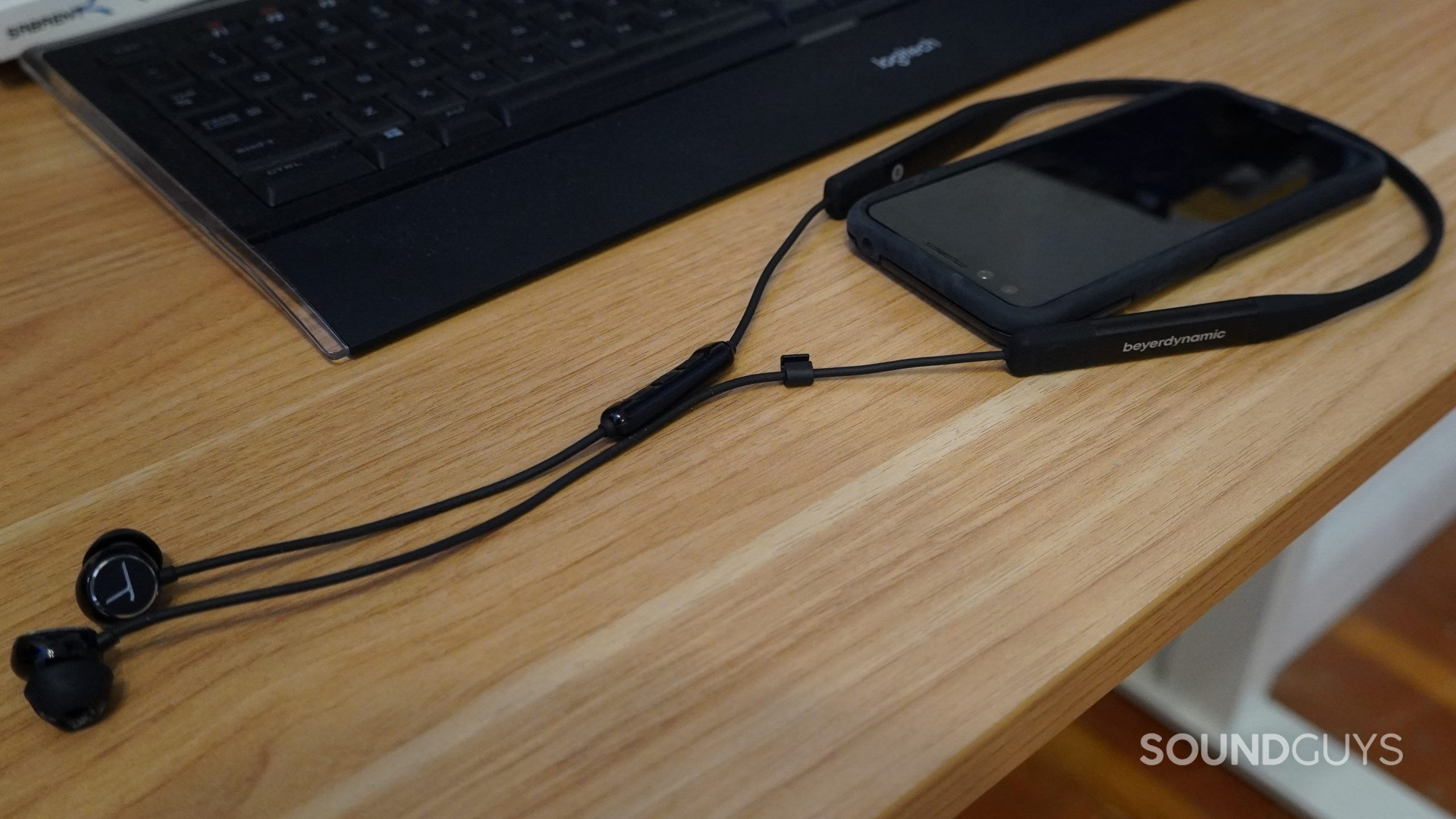 The beyerdynamic Blue Byrd 2 lying on a table looped around a smartphone in front of a black computer keyboard.