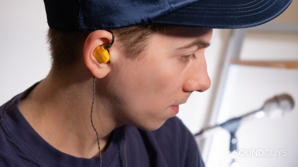 A man looks to the right while wearing the Campfire Audio Honeydew in ears with a microphone in the background.