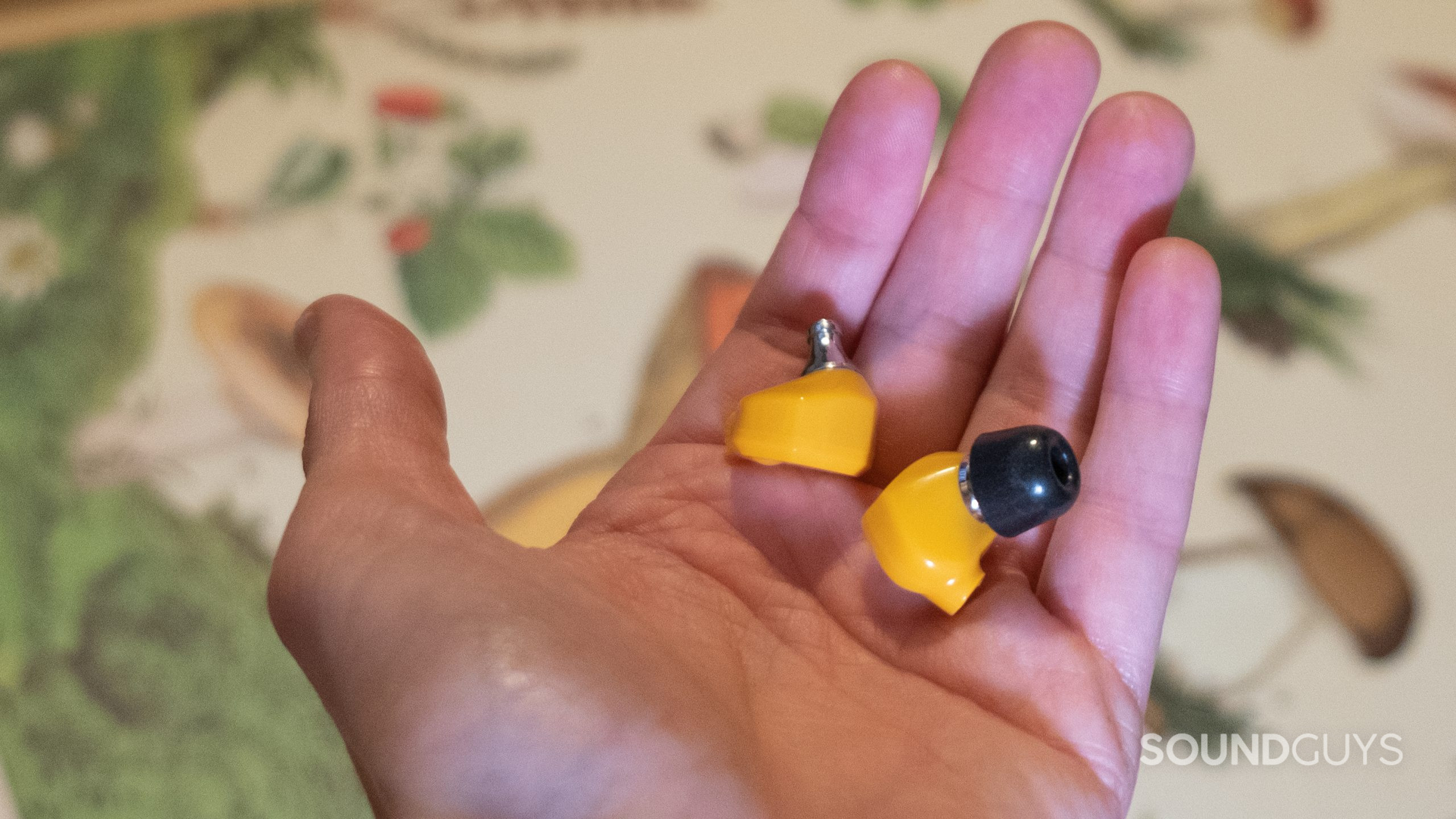 A hand holds both Campfire Audio Honeydew buds. One bud does not have the ear tip to show the metal stem.