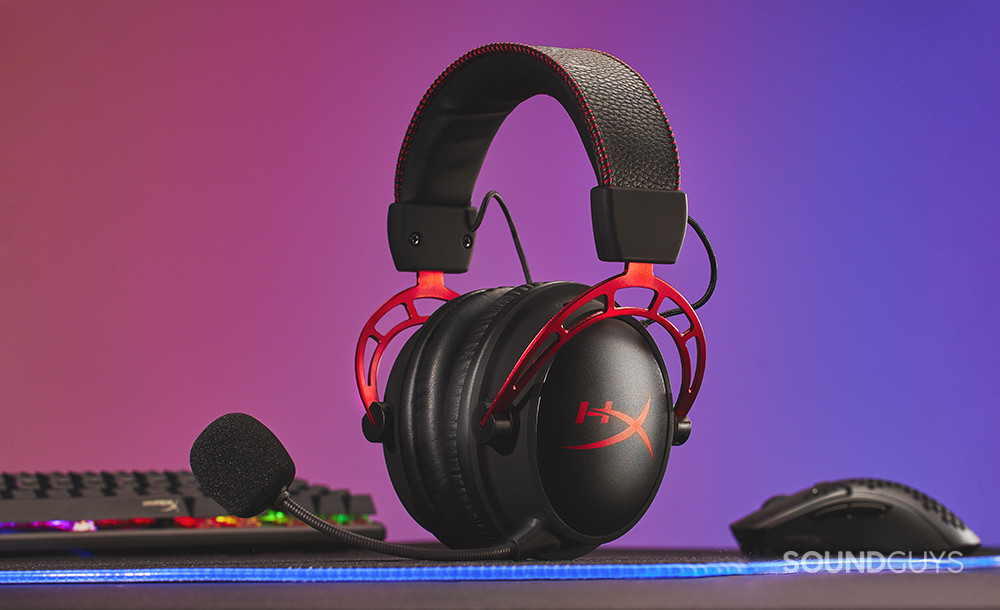 The HyperX Cloud Alpha Wireless sits atop a desk with a pink, purple, and blue backdrop.