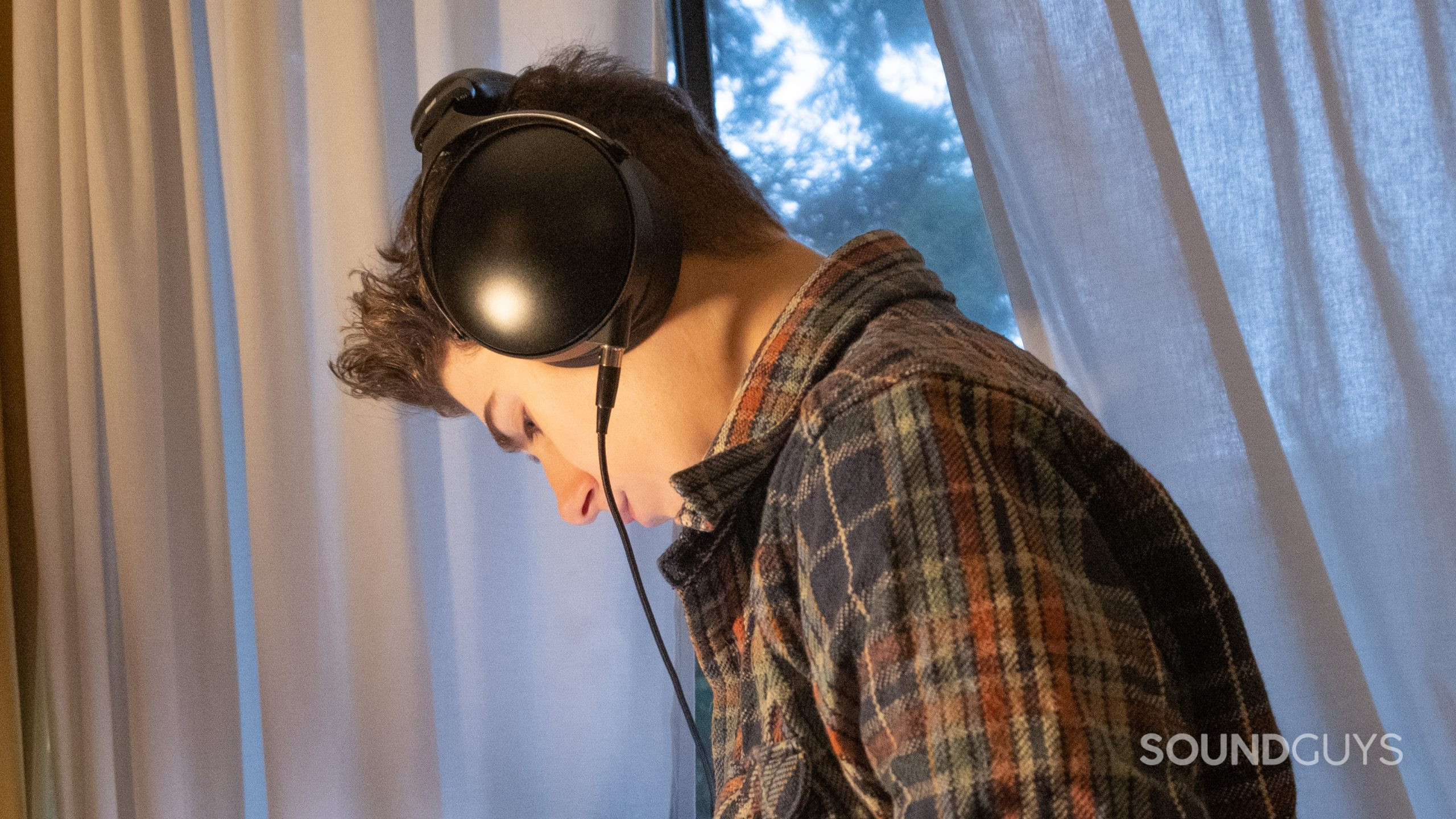 A man shot from the side looks down in front of curtains while wearing the Monolith by Monoprice M1570C.