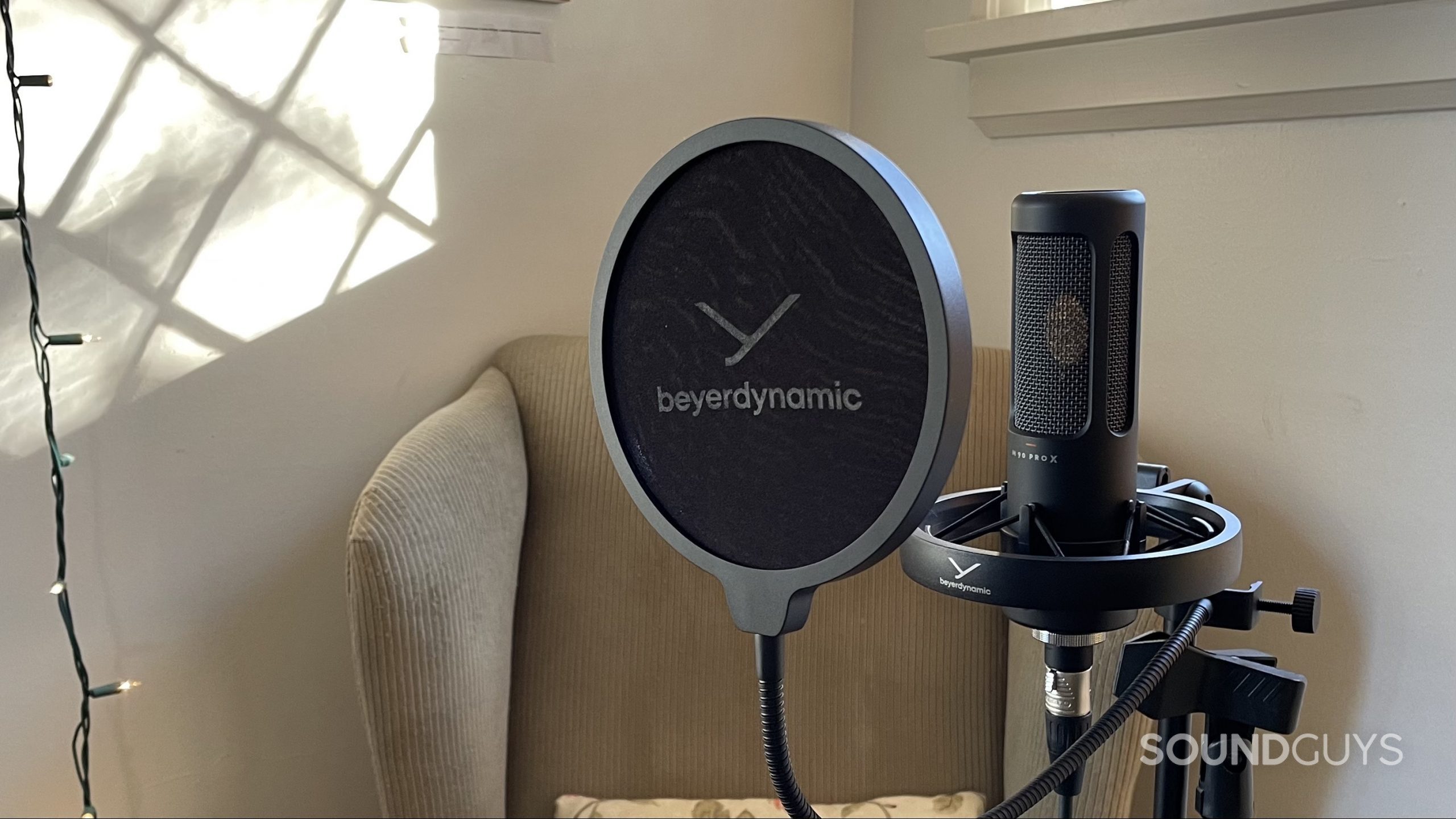 Beyerdynamic M90 PRO X with its pop filter and an armchair and string lights in the background.