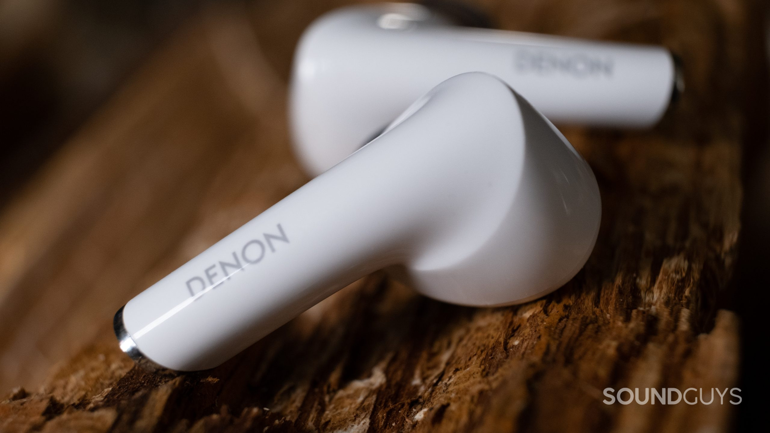 The Denon AH-C830CNW earbuds in close up resting on rough wood.