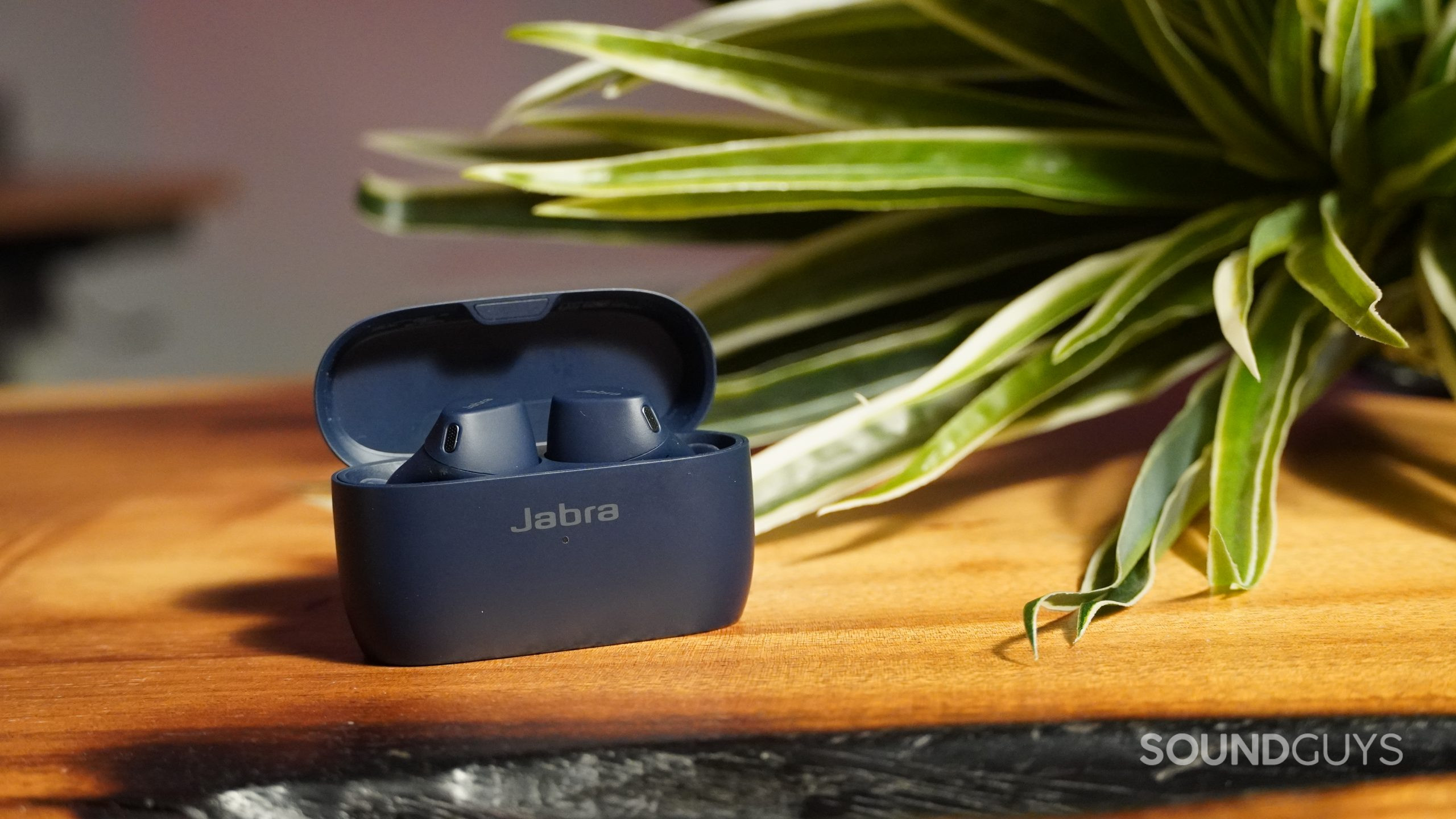Jabra Elite 4 Active earbuds on table next to plant with red light in background.